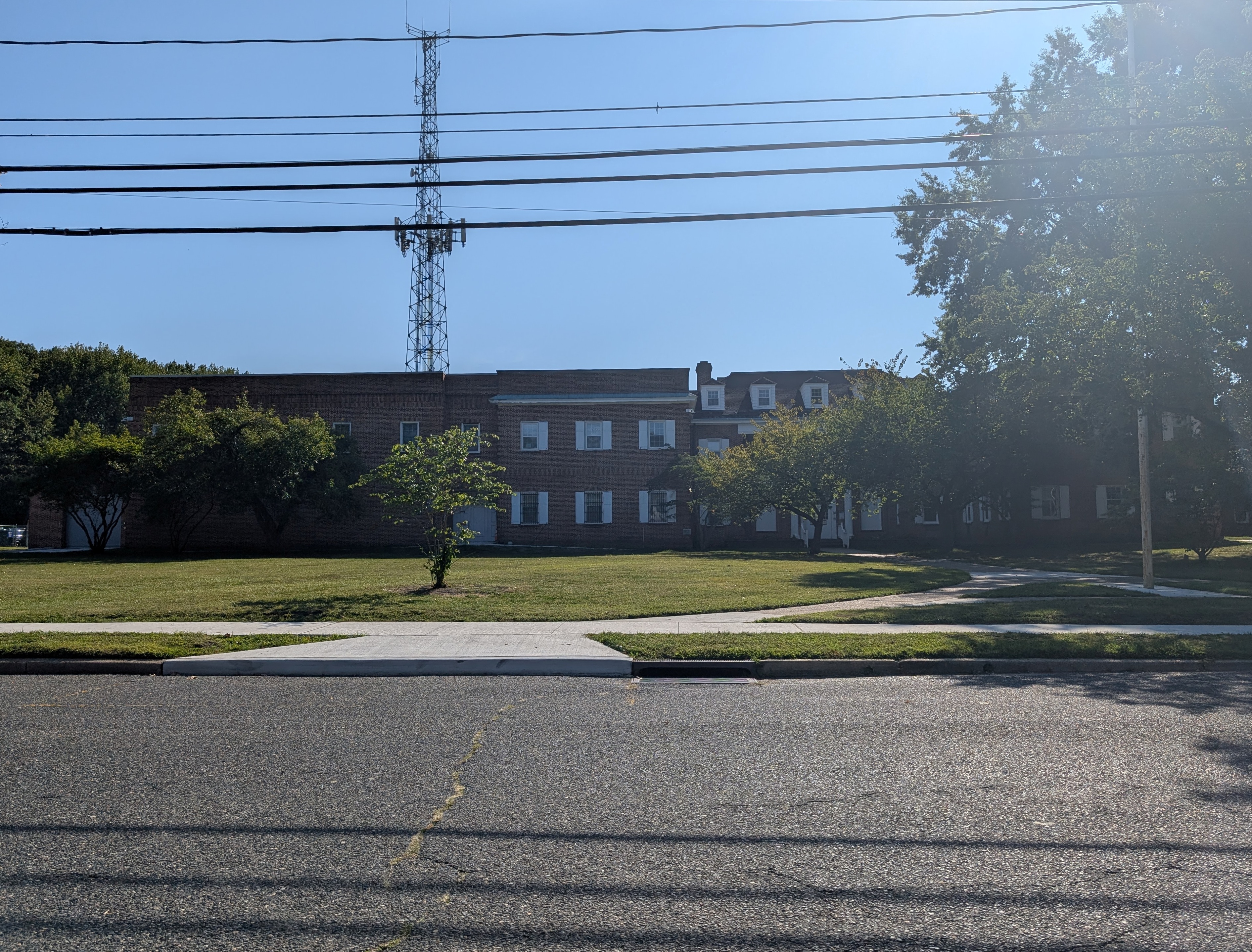Two-story red brick municipal building with a large lawn and trees on a sunny day.