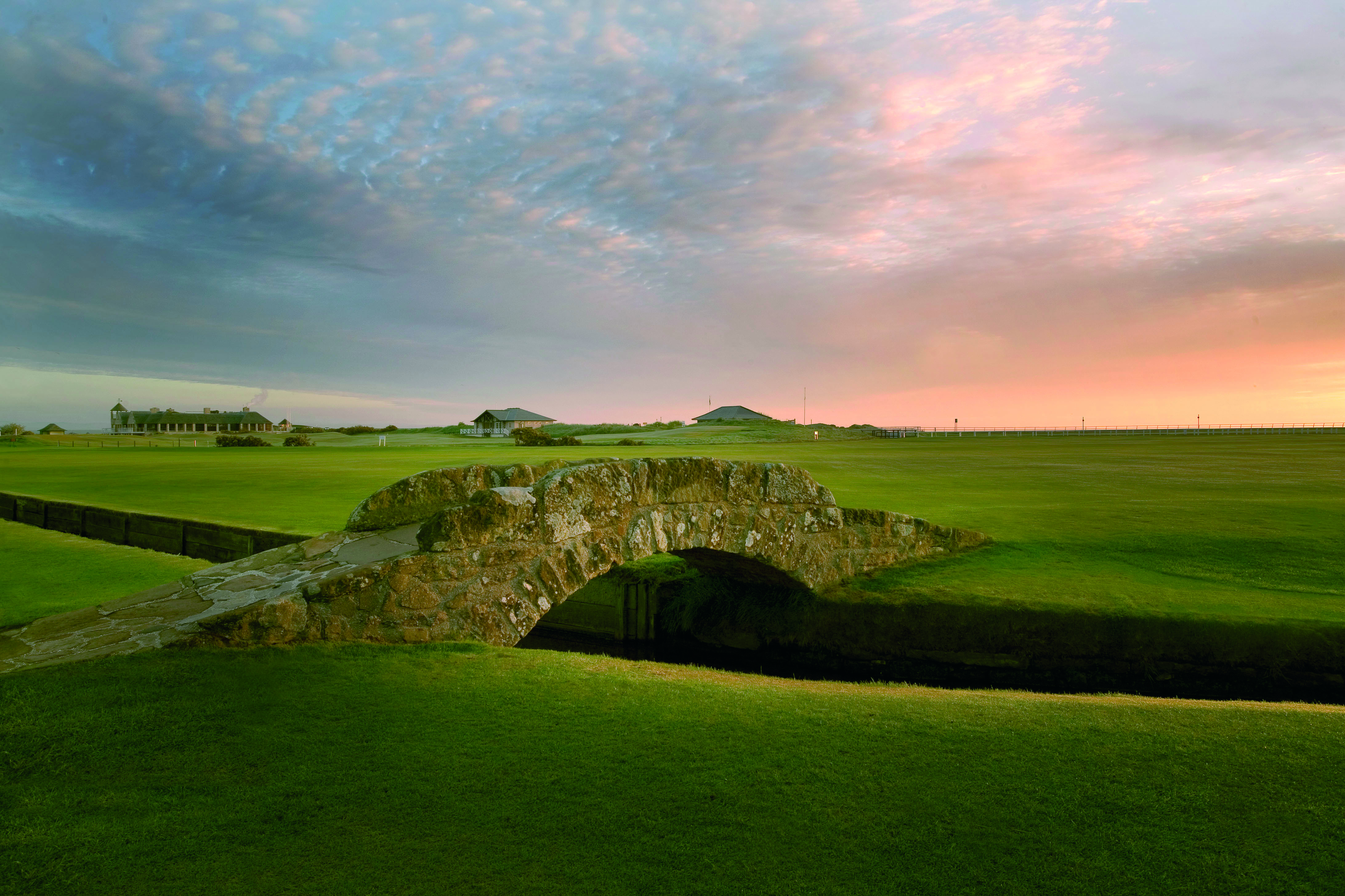 Stone arch bridge crossing a burn on a golf course fairway at sunset.