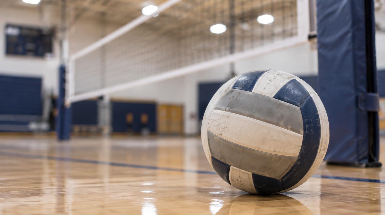 A volleyball resting on a hardwood gymnasium floor near the net post.