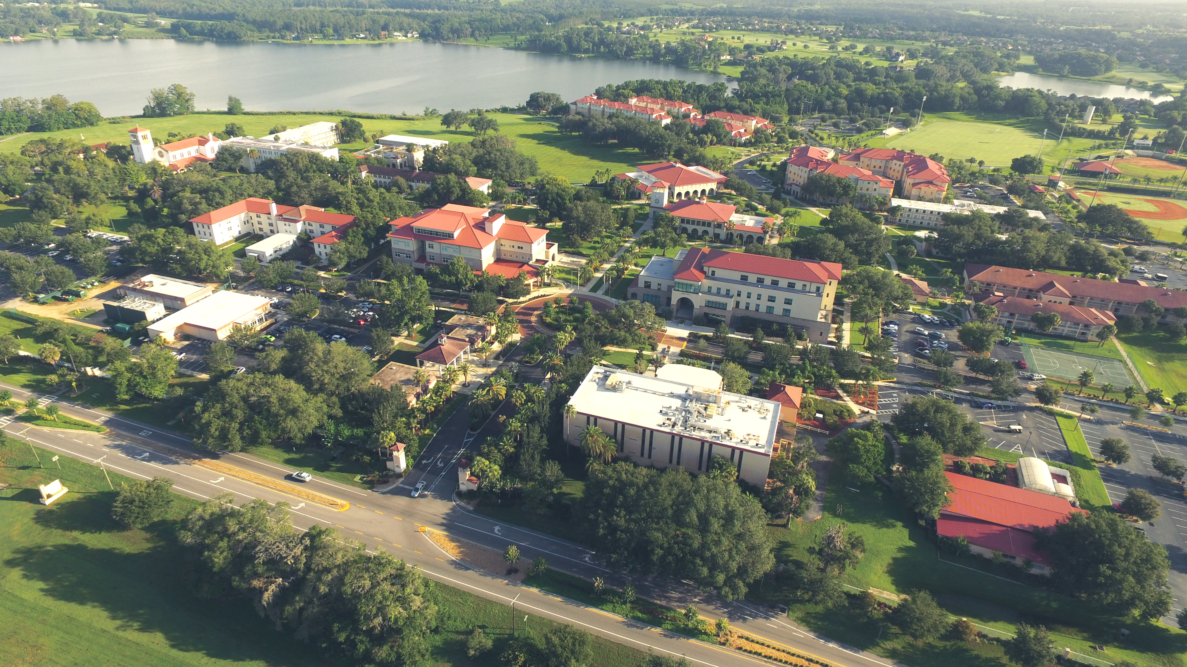 Aerial view of a university campus with red-roofed buildings, green lawns, and a lake.