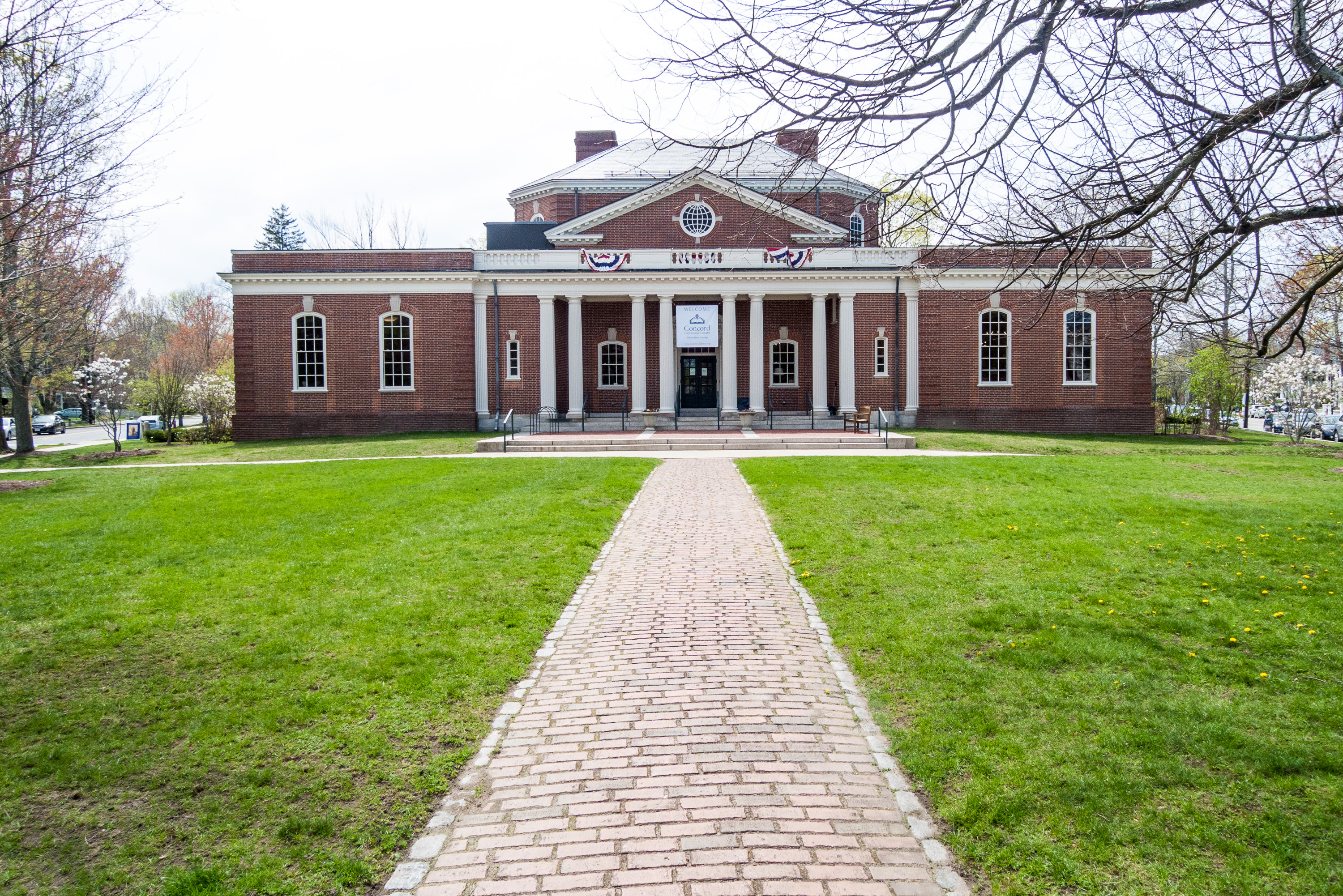 Brick neoclassical library building with white columns and a green lawn in front.
