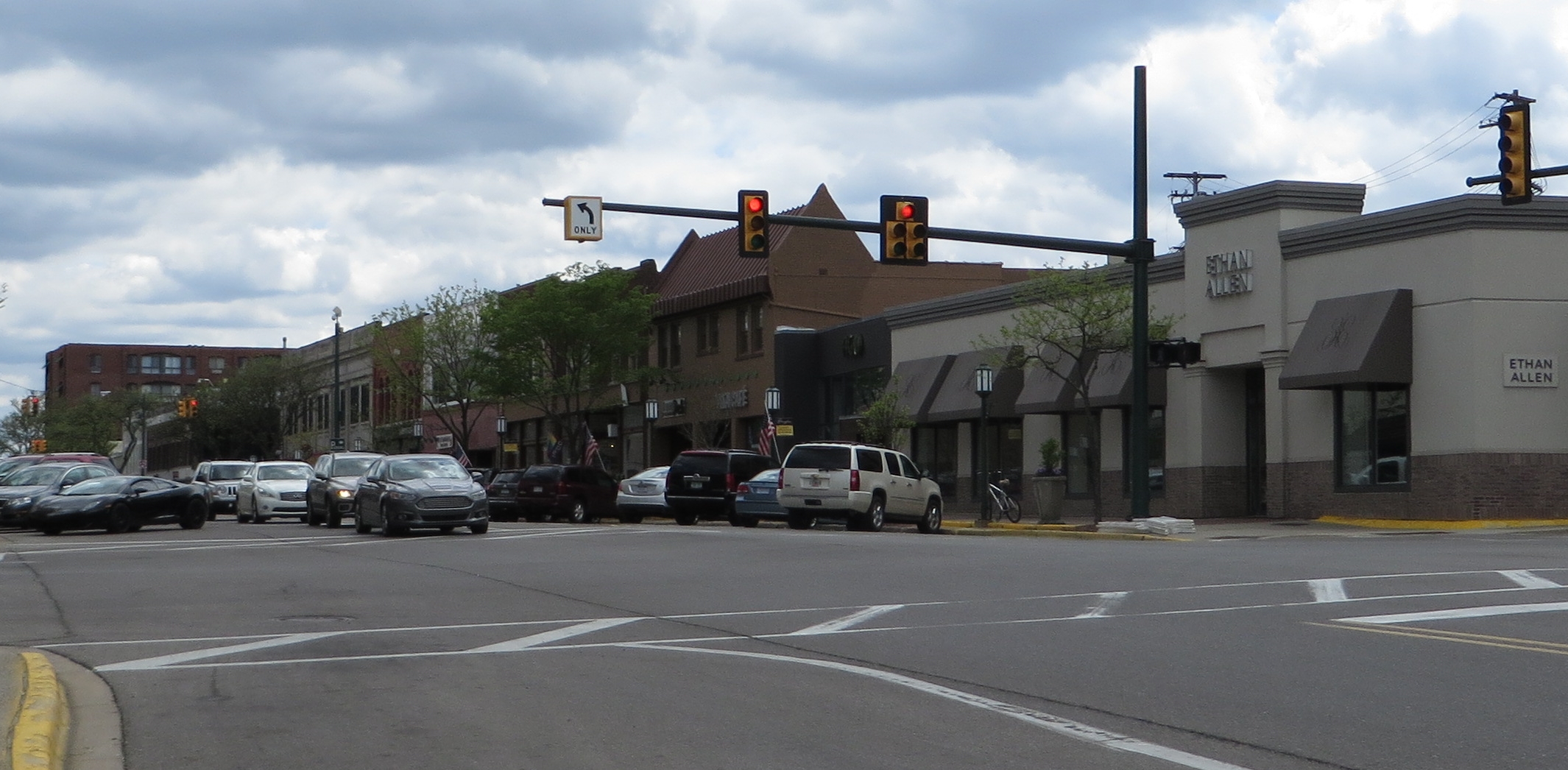 Signalized street intersection lined with storefronts and parked cars in a downtown district.