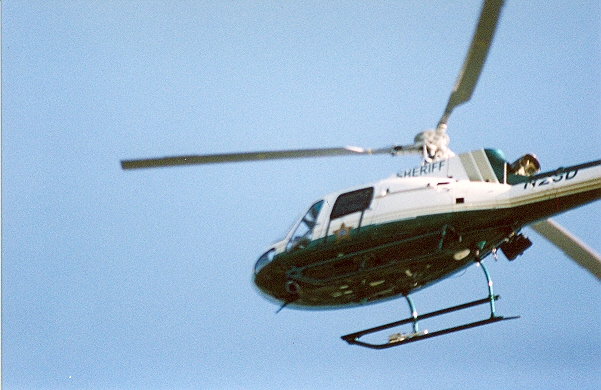 White and dark green sheriff's helicopter in flight against a clear blue sky.