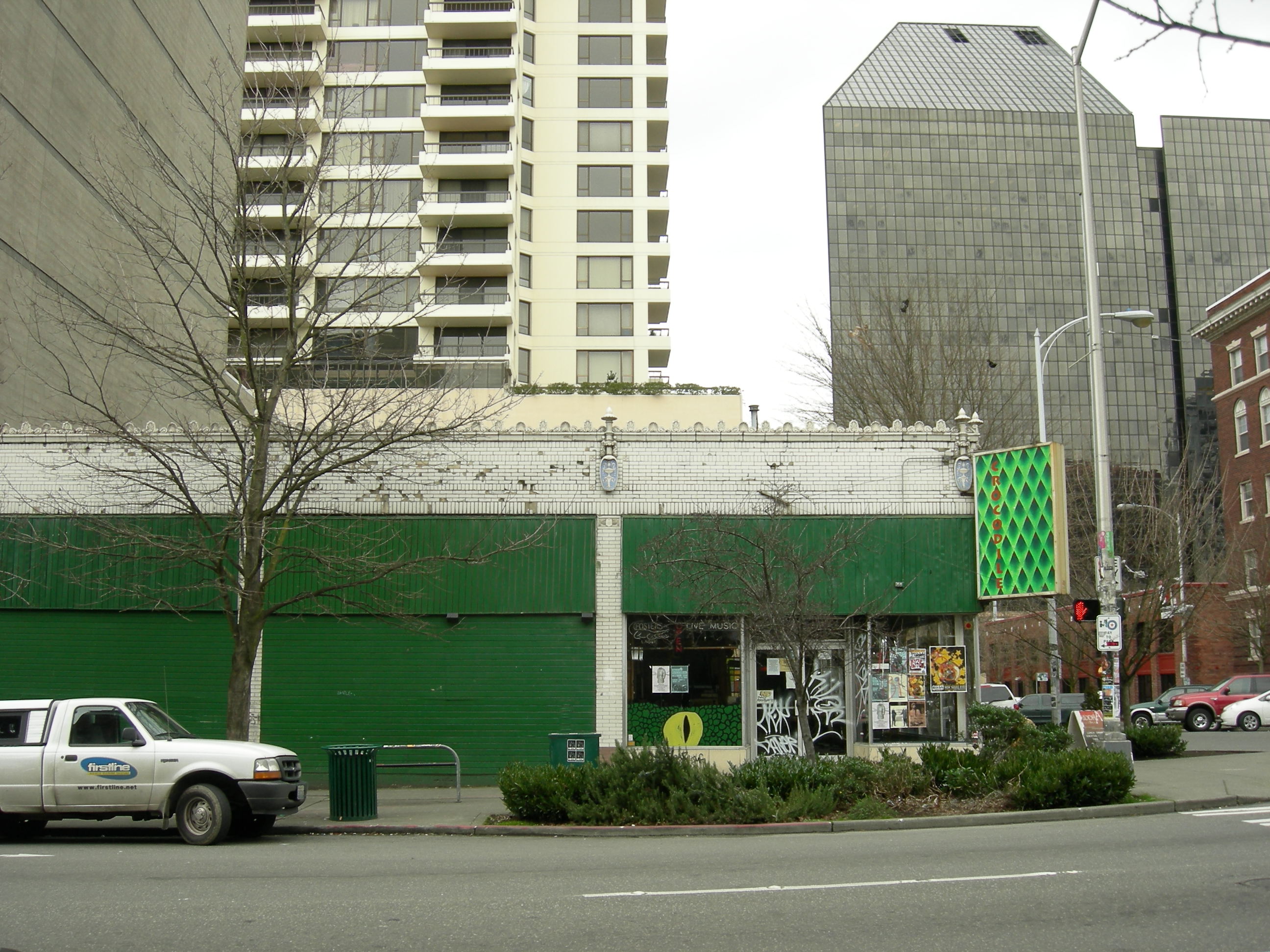 Low-rise green building with metal shutters on a Seattle street, tall tower behind it.