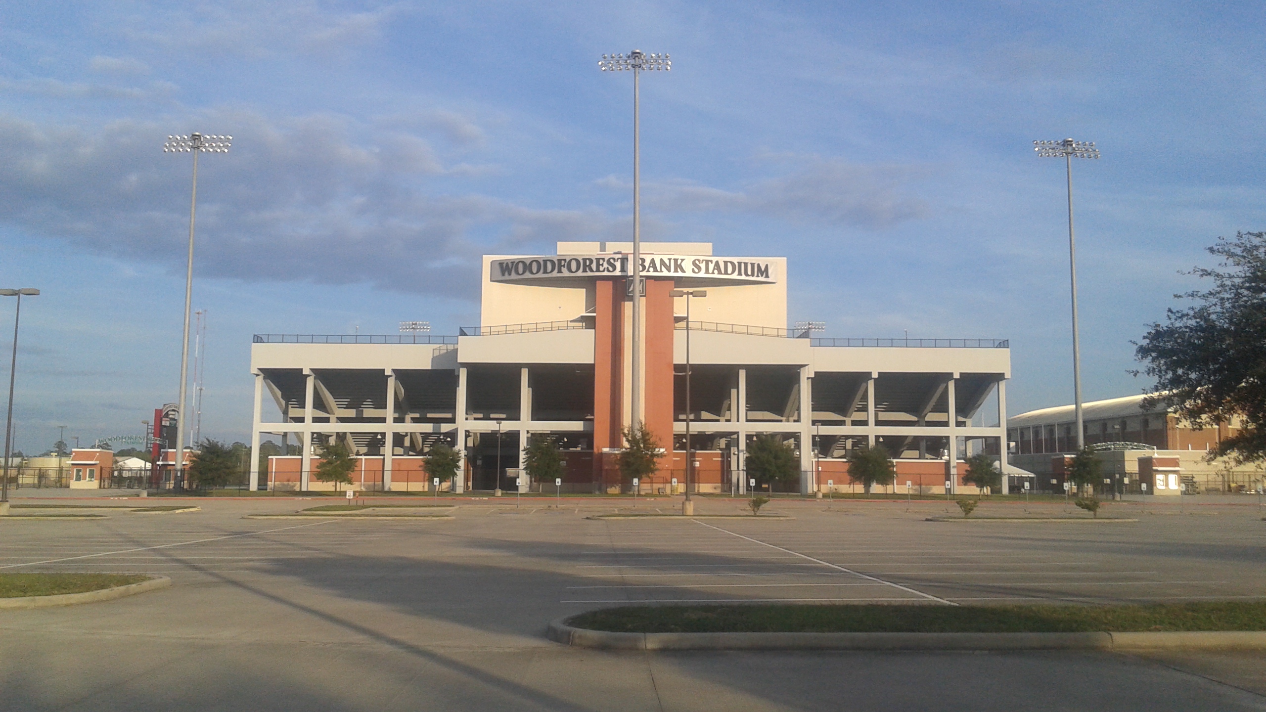 Exterior facade of a large high school football stadium with tall light towers and prominent signage.