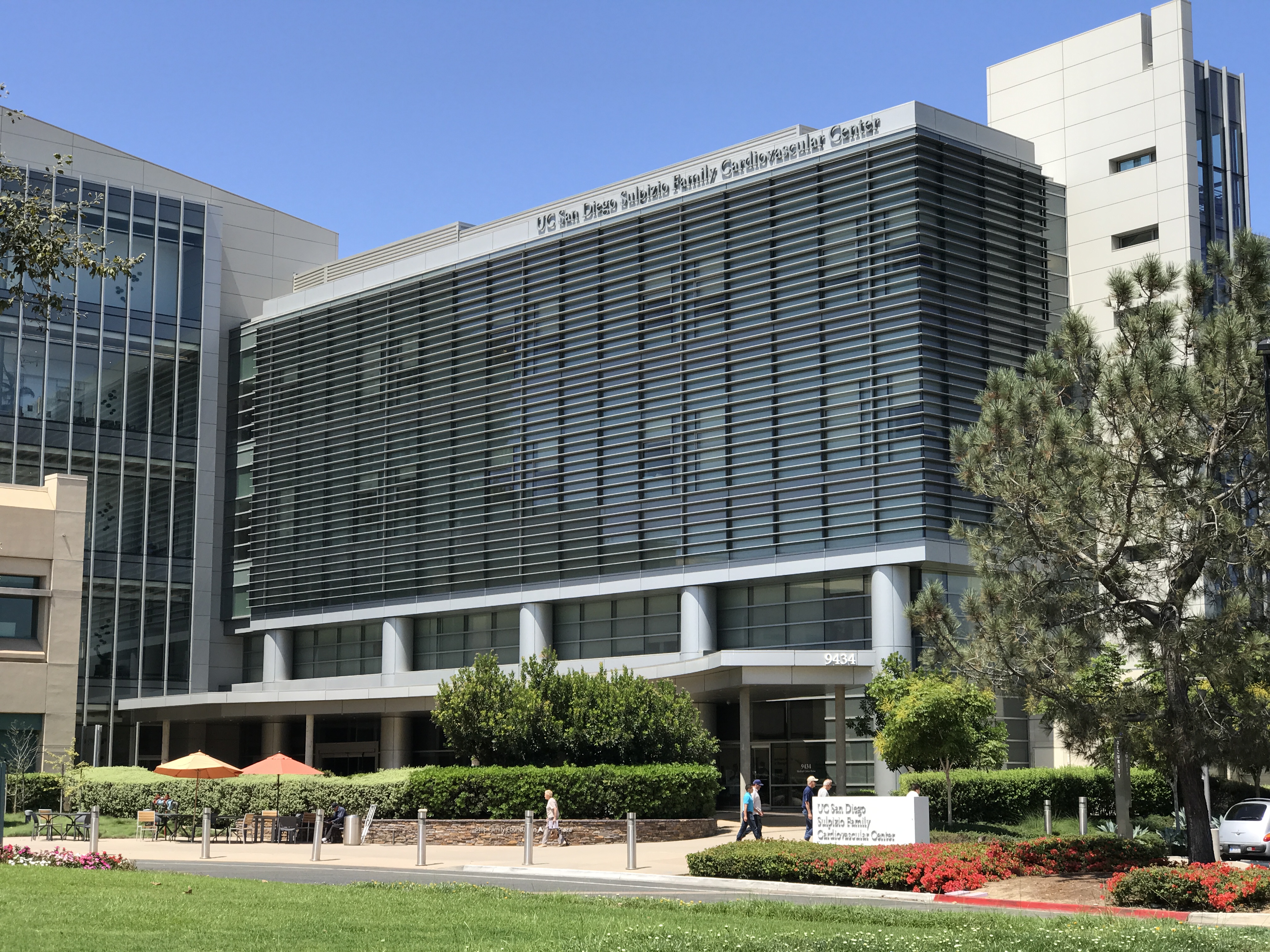 Modern multi-story glass and concrete building on a university health campus surrounded by trees.