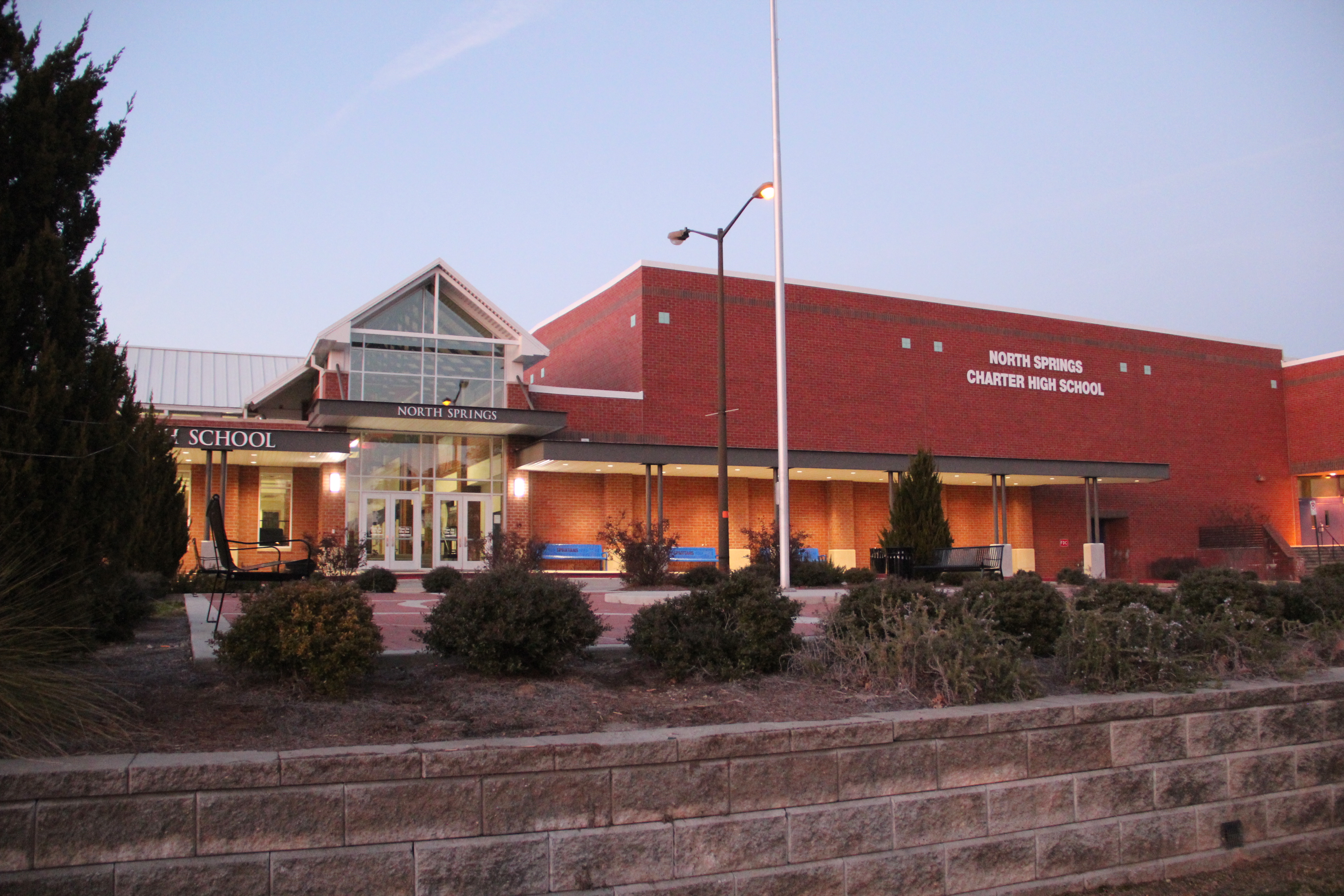 Red-brick high school building exterior at dusk with flagpole and landscaping.