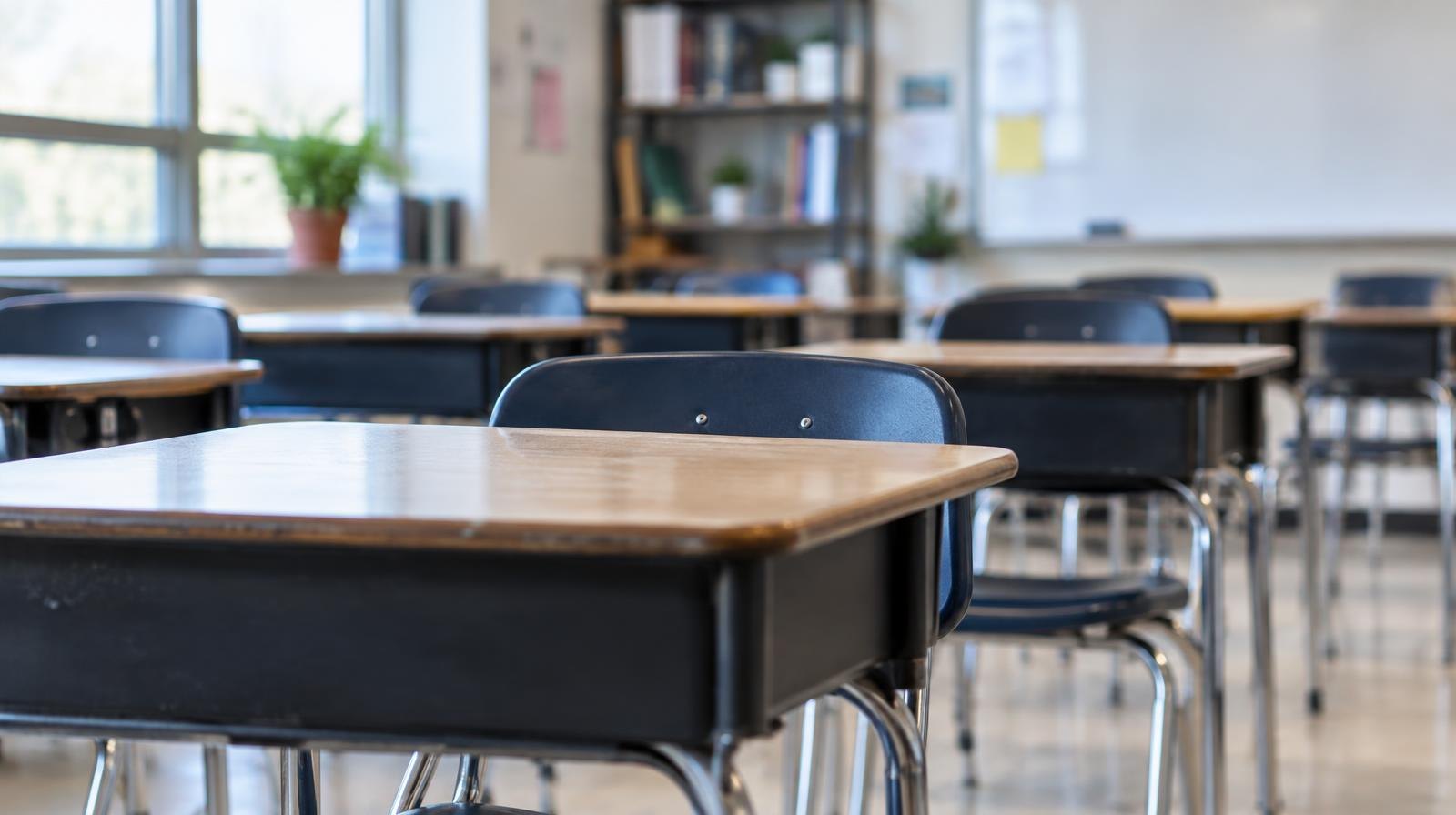 Rows of empty student desks in a bright, modern school classroom.