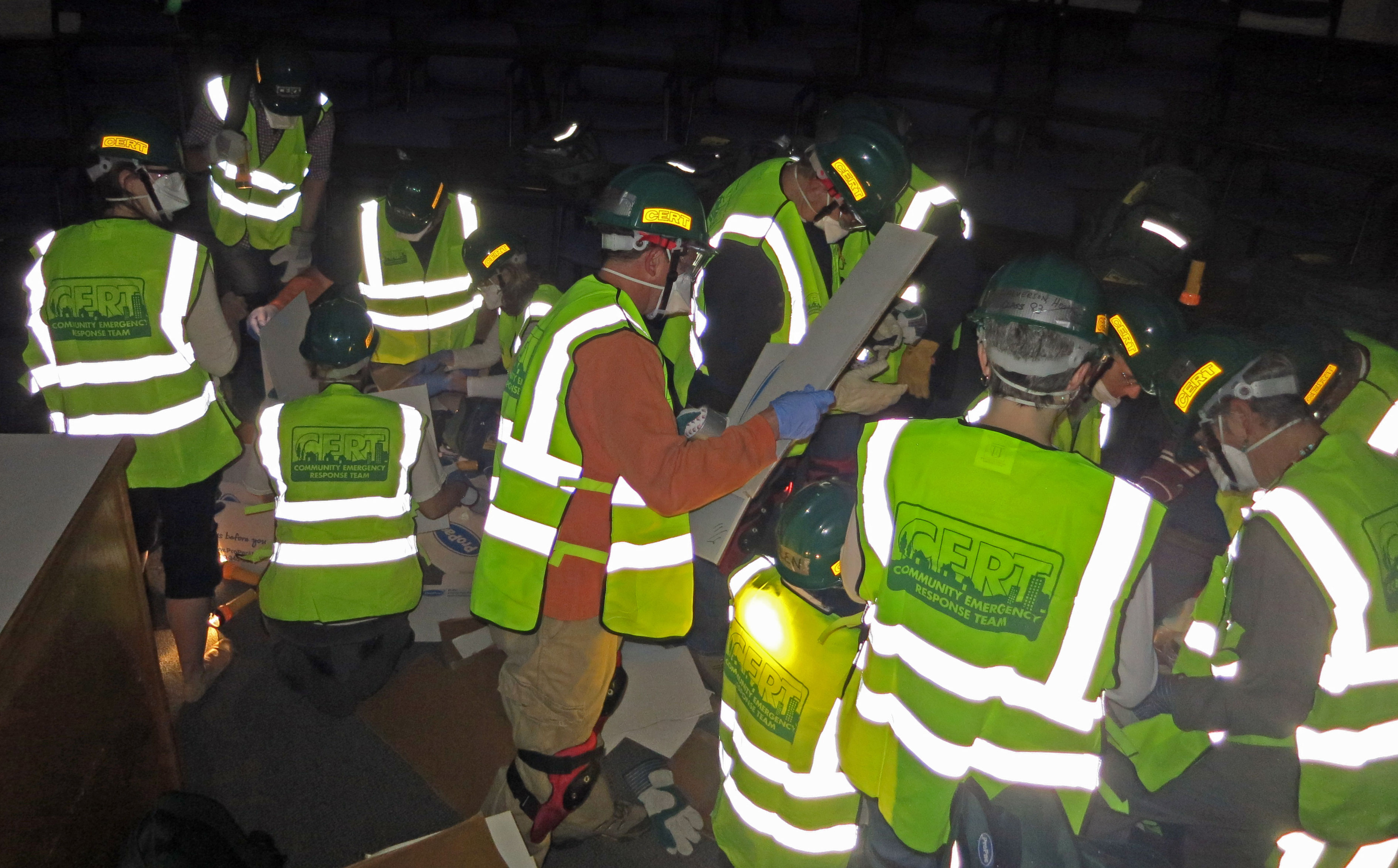 Volunteers in yellow CERT vests and green hard hats with headlamps conduct an indoor training drill.