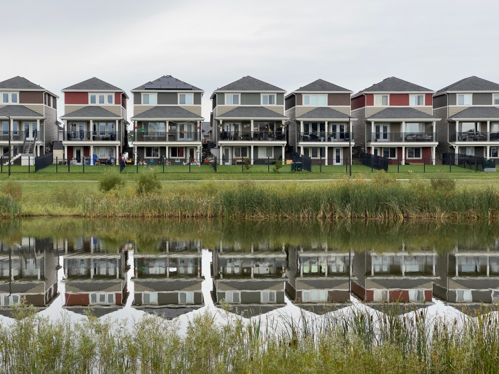 A row of modern houses reflected in a calm pond, showcasing serene suburban architecture.