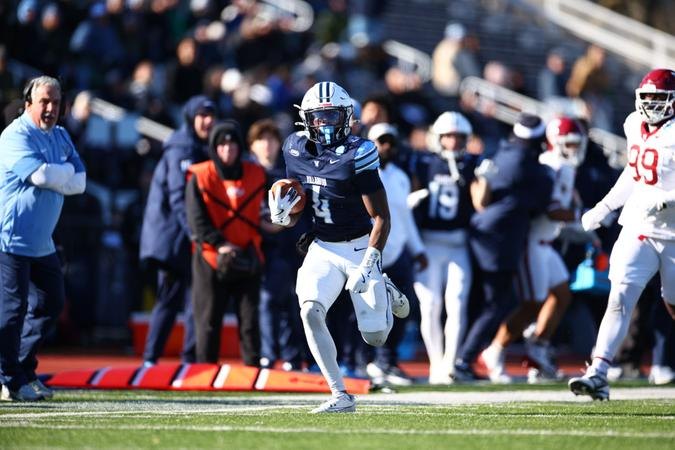 Villanova football player in navy uniform carrying the ball along the sideline during a game.