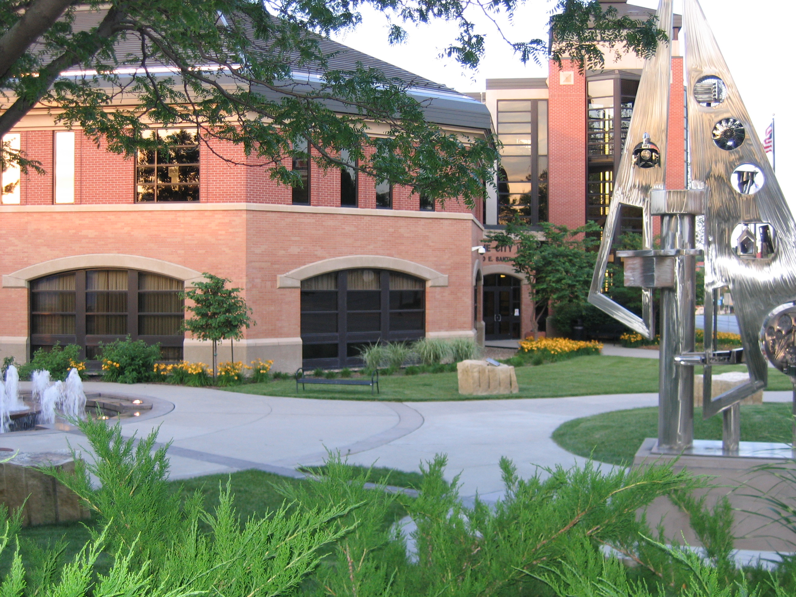 Brick municipal building with arched windows, fountain, and manicured plaza at dusk.