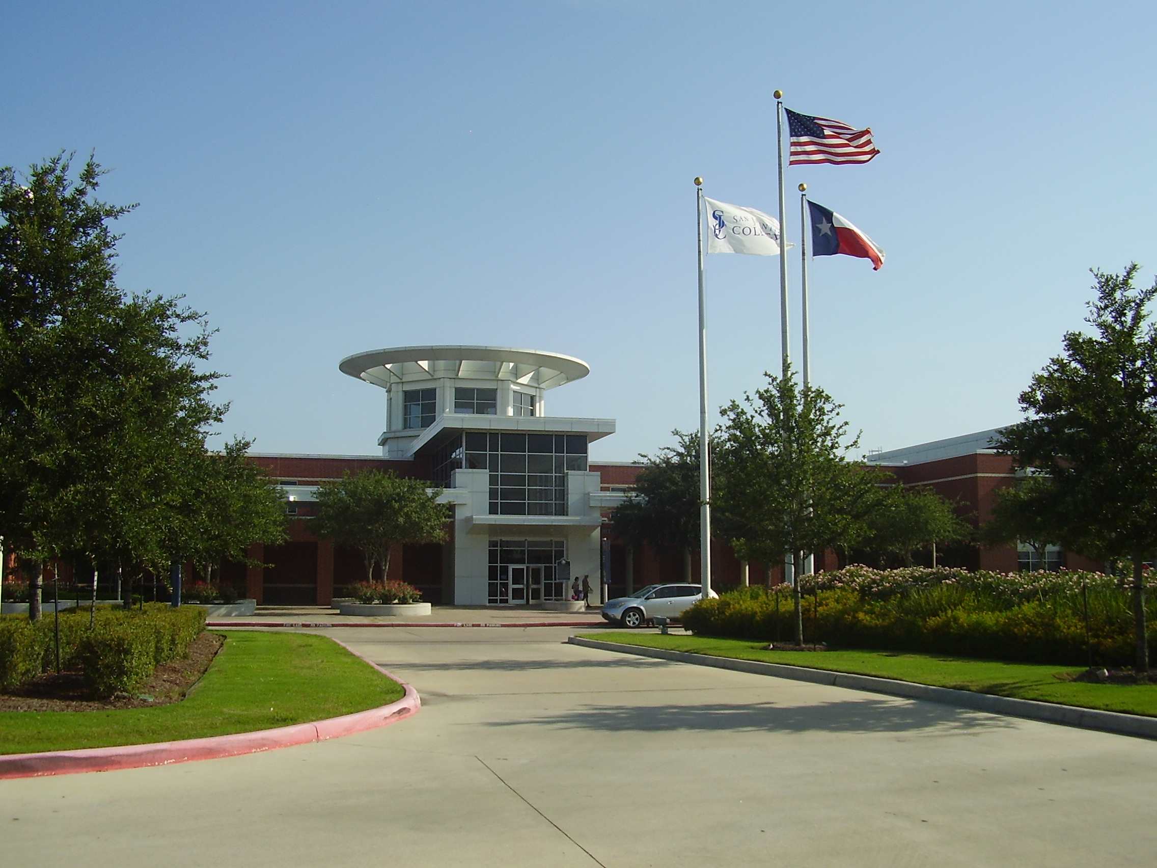 Brick college building with circular upper level and three flagpoles under a clear sky.