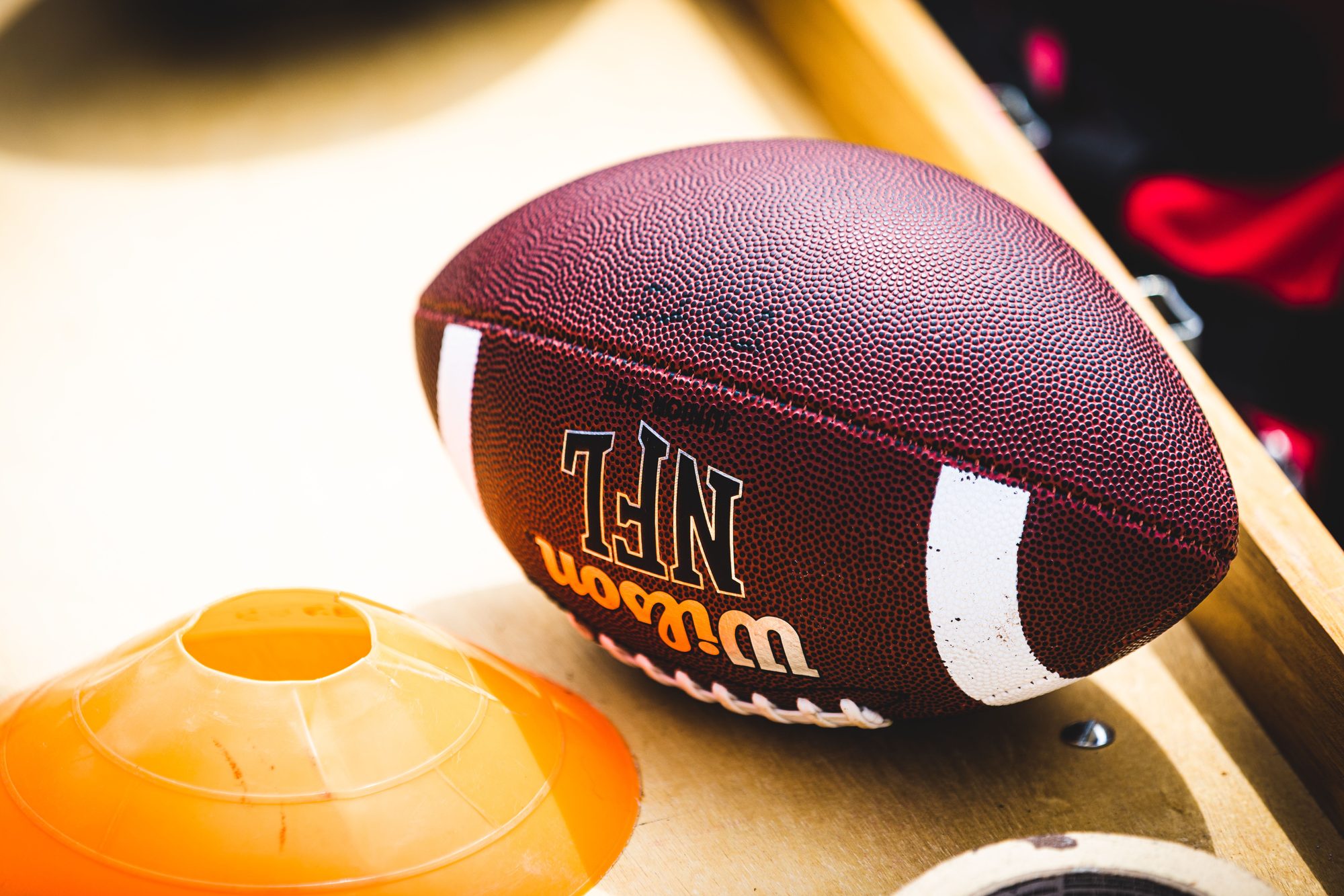 An American football placed on a training bench next to an orange training cone, ideal for sports concept.