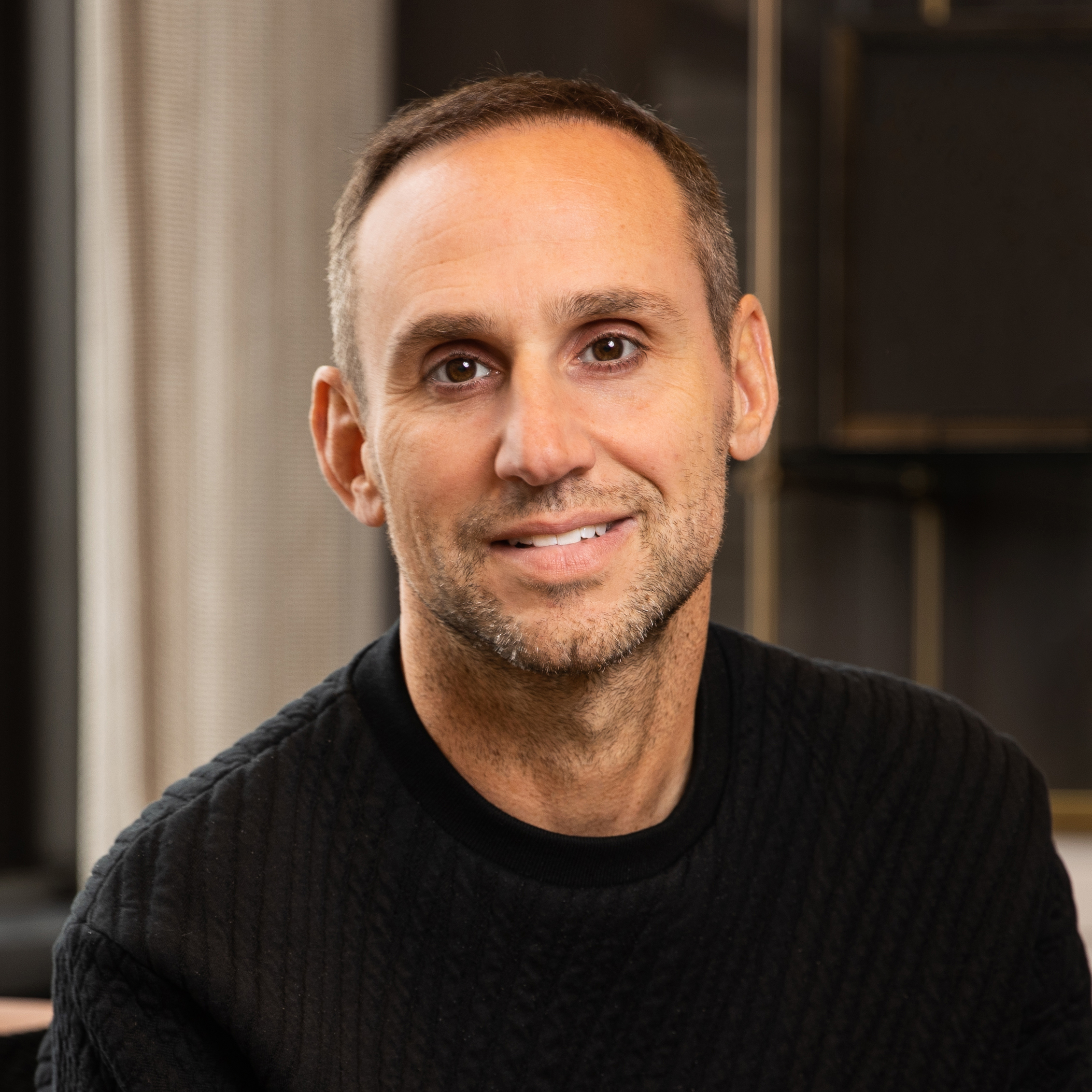 Man in a black cable-knit sweater smiling in a professional portrait.