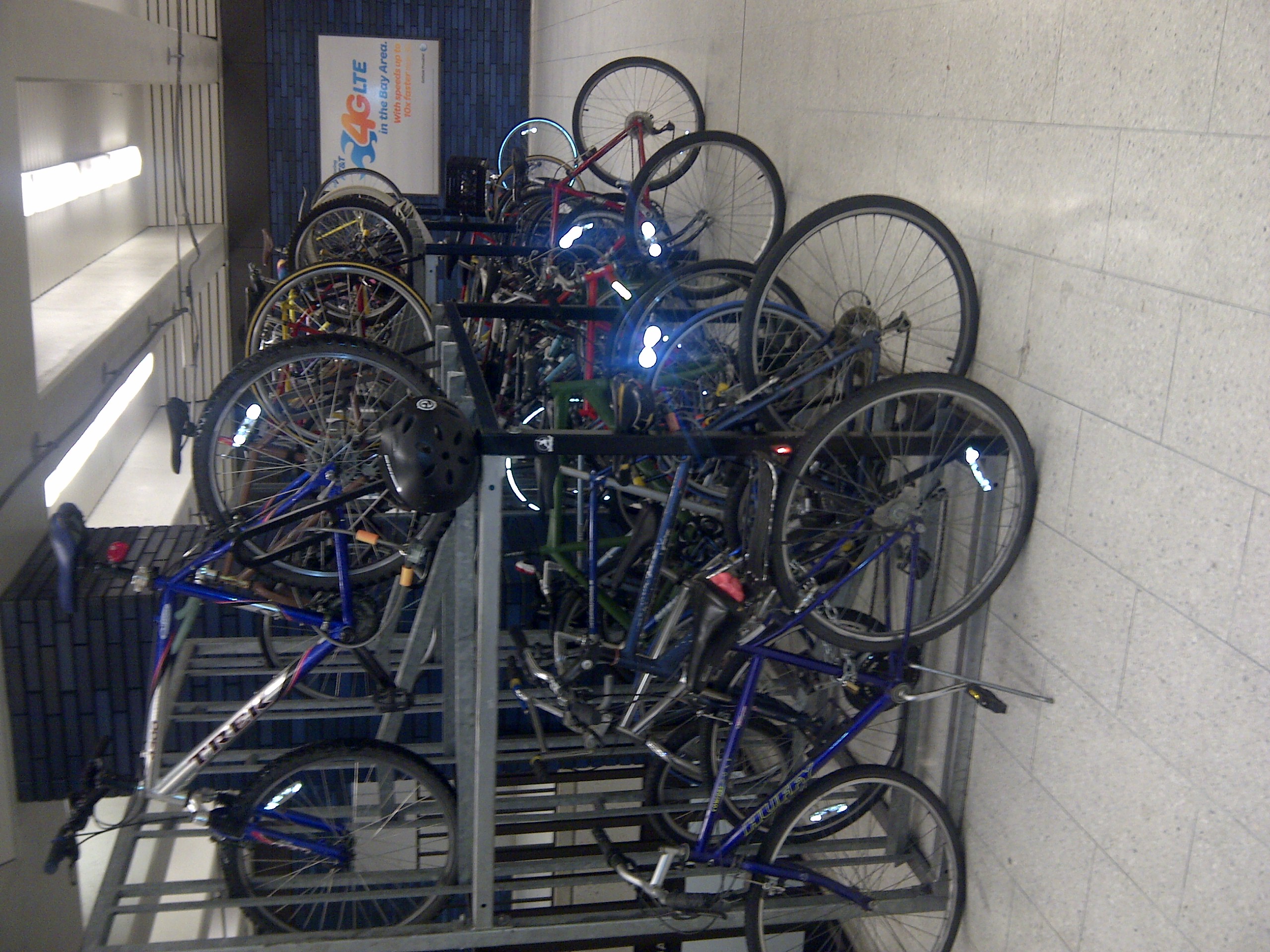 Multiple bicycles parked in a two-level metal rack under fluorescent station lighting.