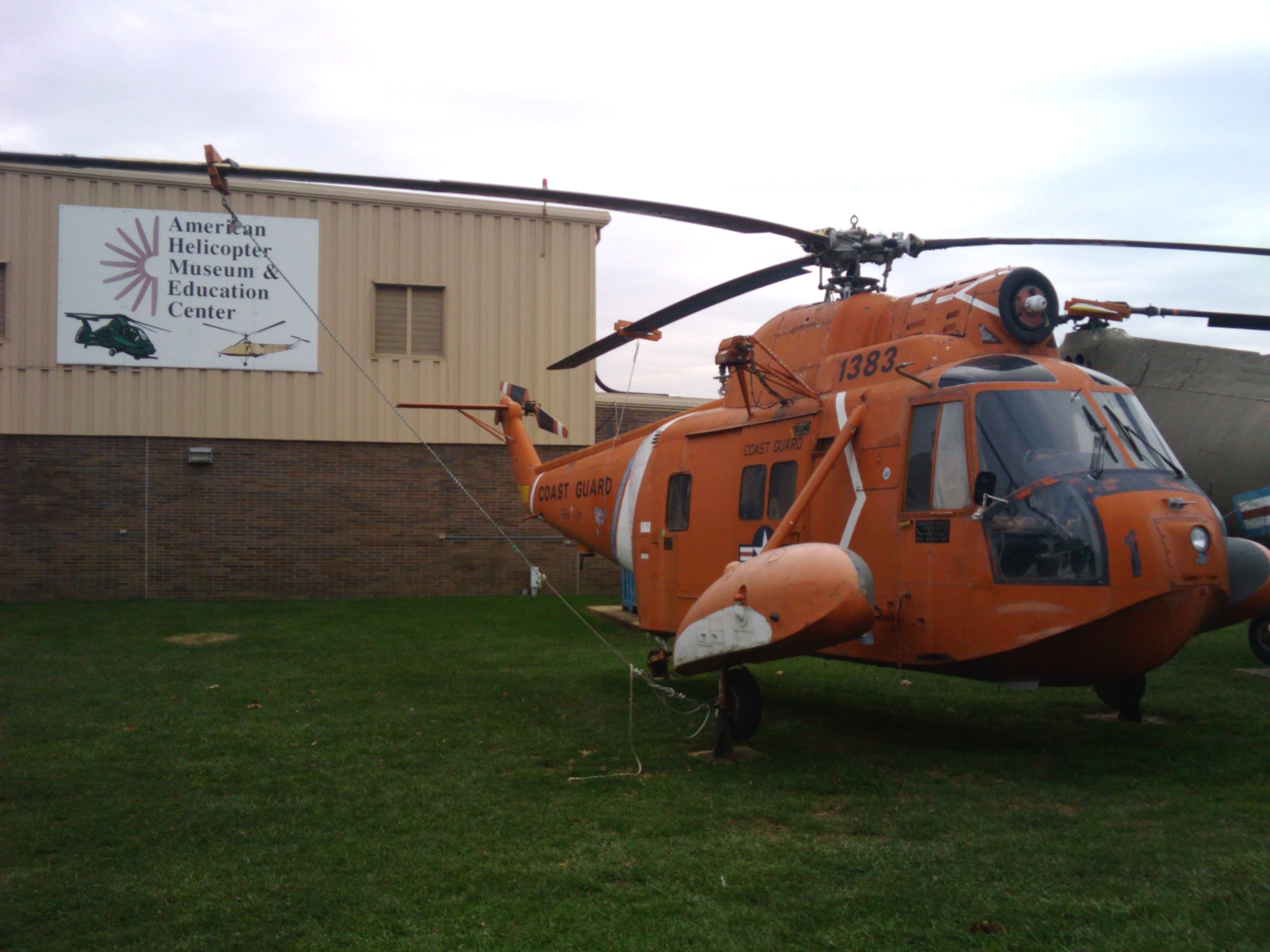 Orange helicopter on grass in front of a museum building with a sign.