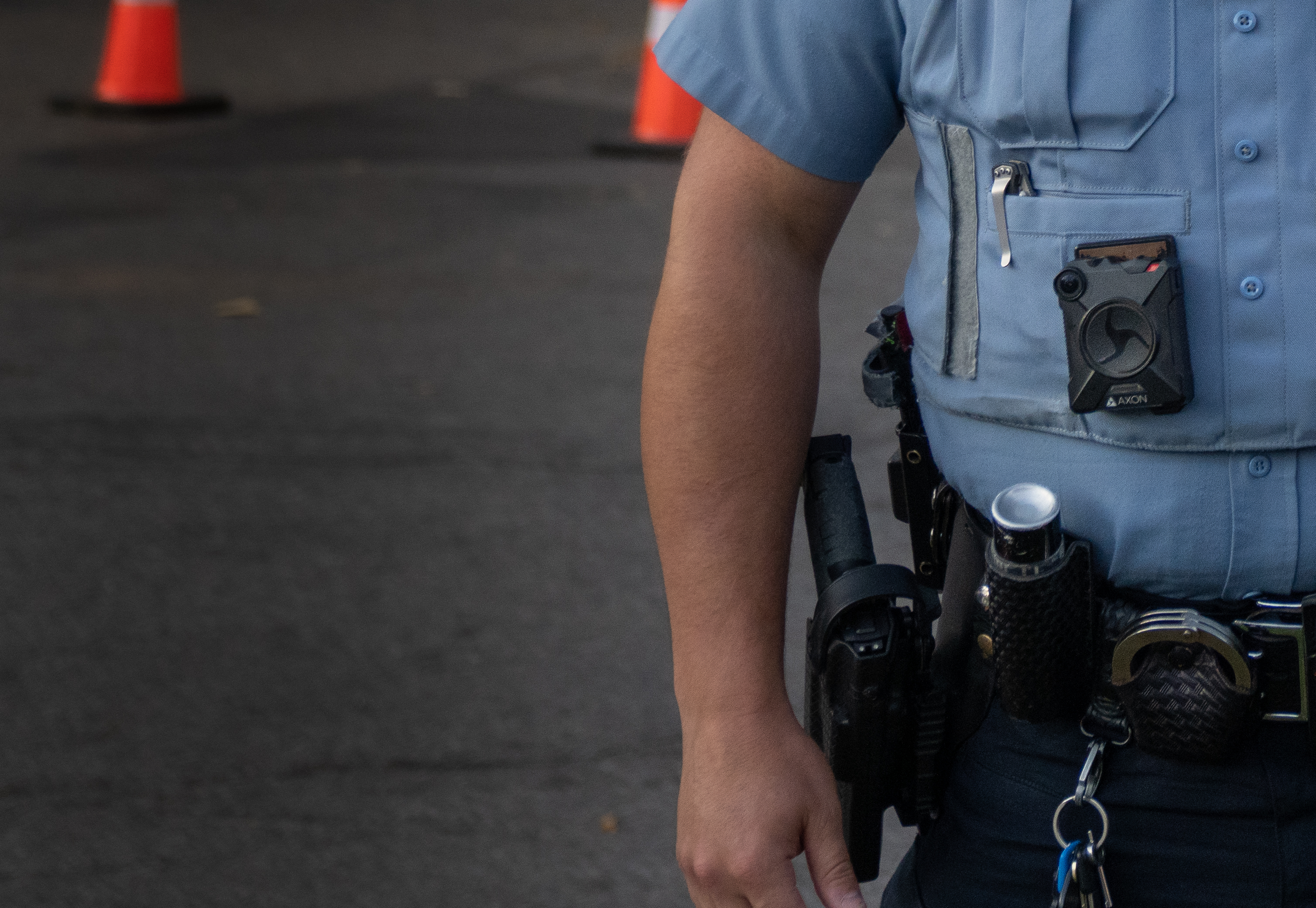 A body-worn camera clipped to a light blue police uniform shirt, duty belt visible below.