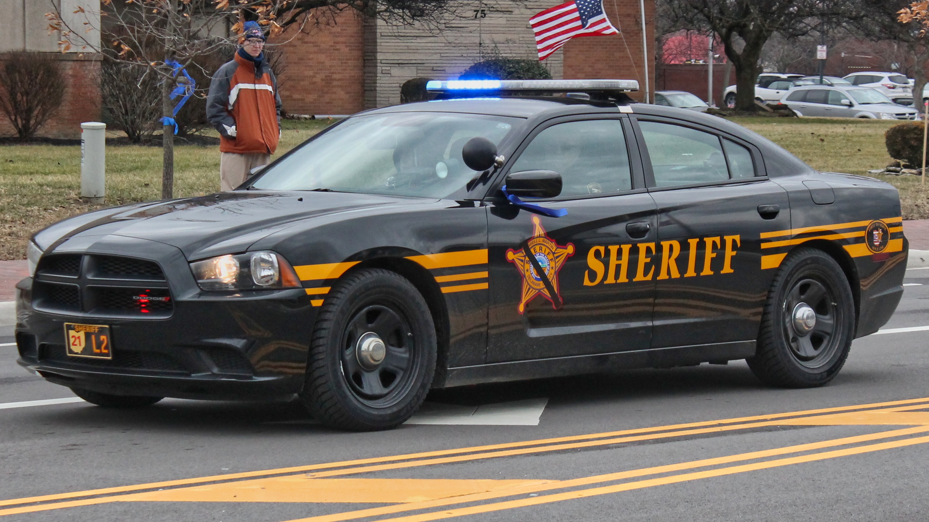 Black and gold sheriff's patrol car with emergency lights flashing on a road.