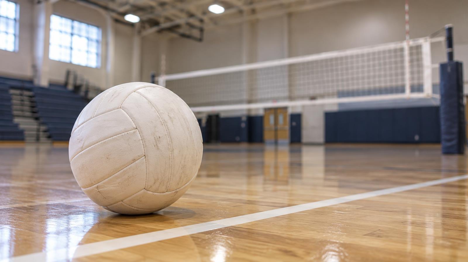 White volleyball resting on a hardwood gym floor near a painted boundary line.