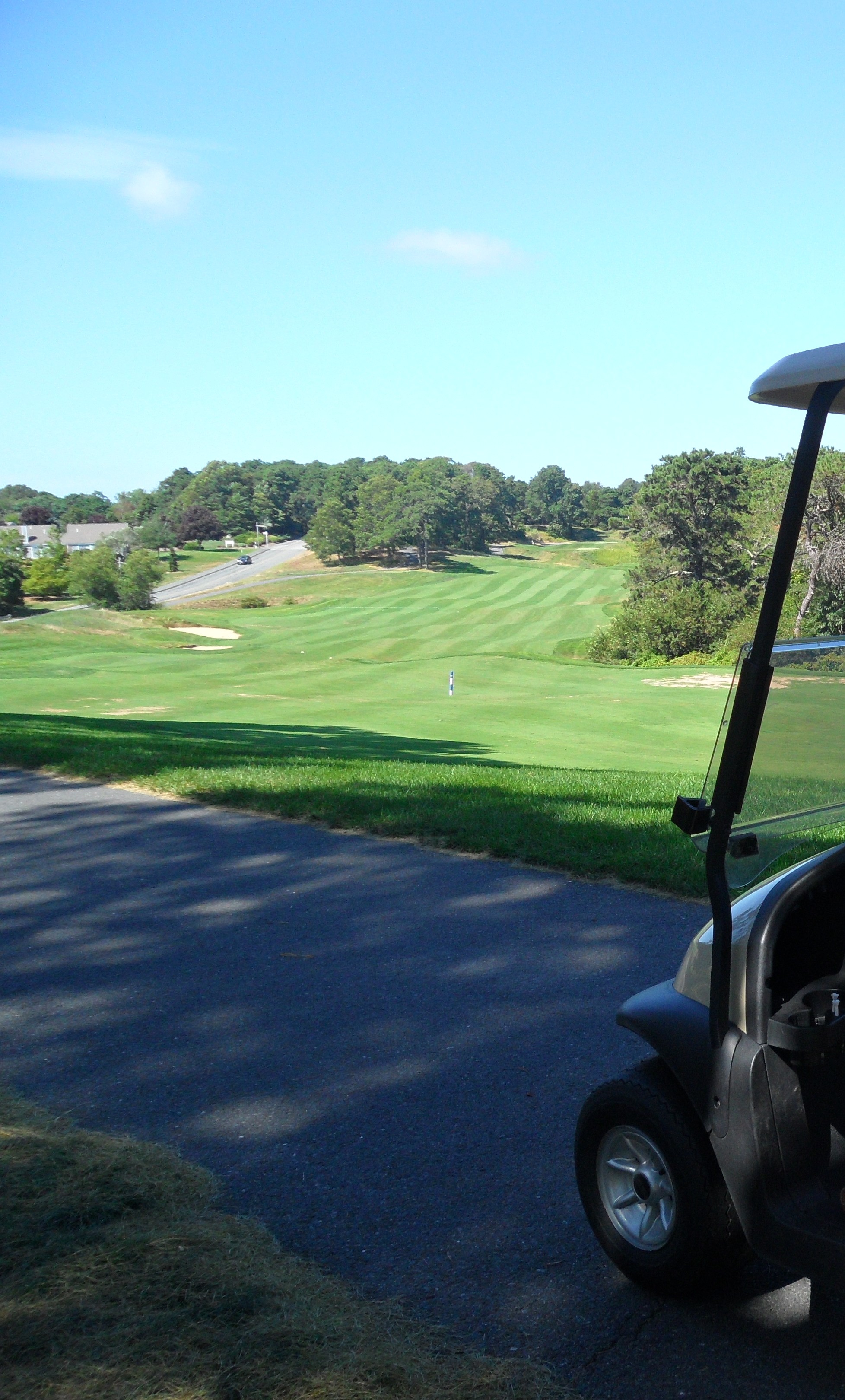 A golf cart parked on a paved path at a golf course on a sunny day.