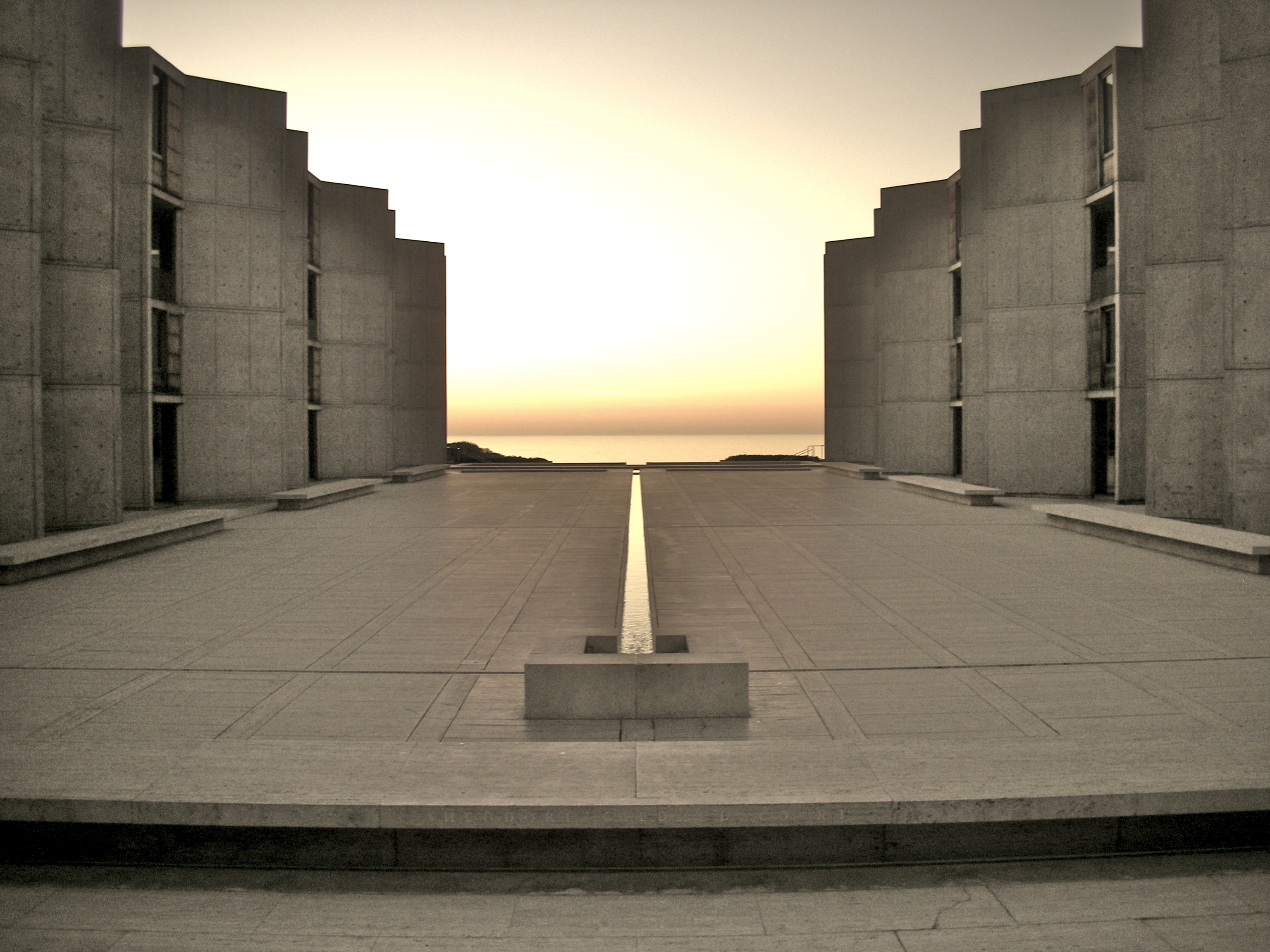 Symmetrical concrete courtyard with a central water channel leading toward the ocean horizon.