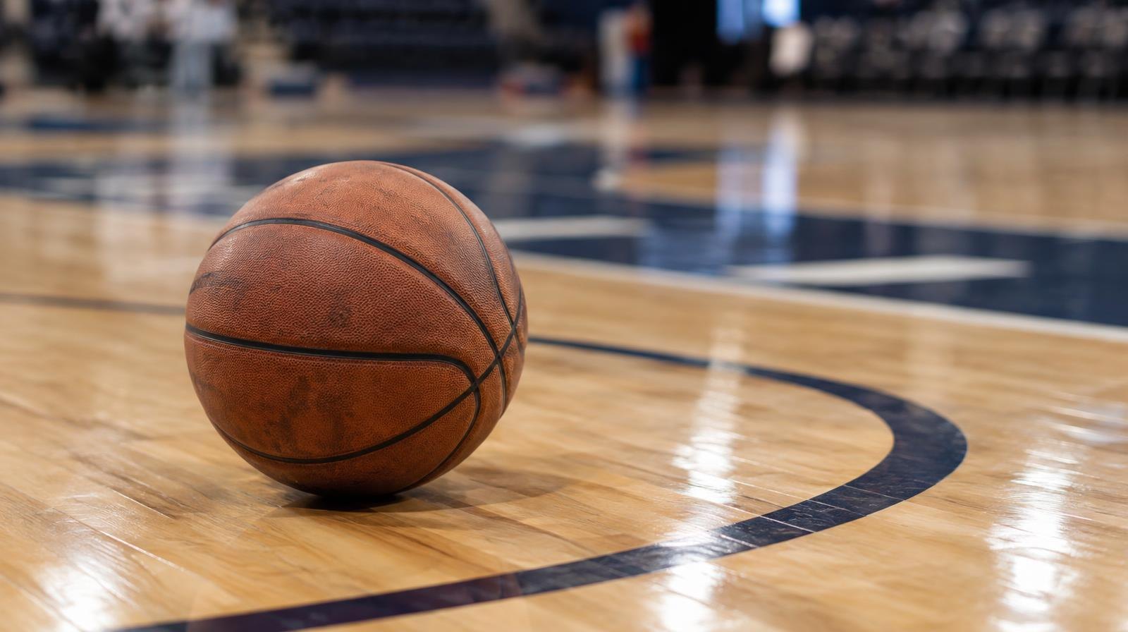 A basketball resting on a painted hardwood court near the three-point line.
