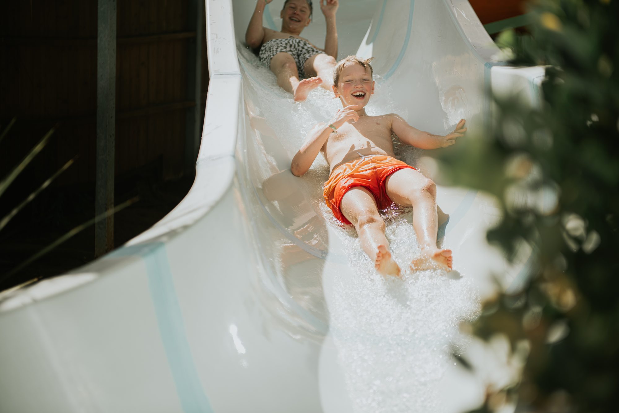 Two children joyfully sliding down a water slide at a water park on a bright sunny day