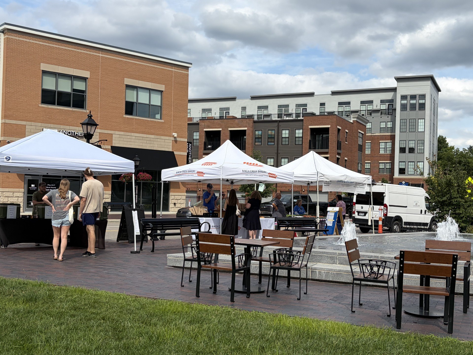 White pop-up canopy tents set up in an outdoor plaza with people browsing nearby.
