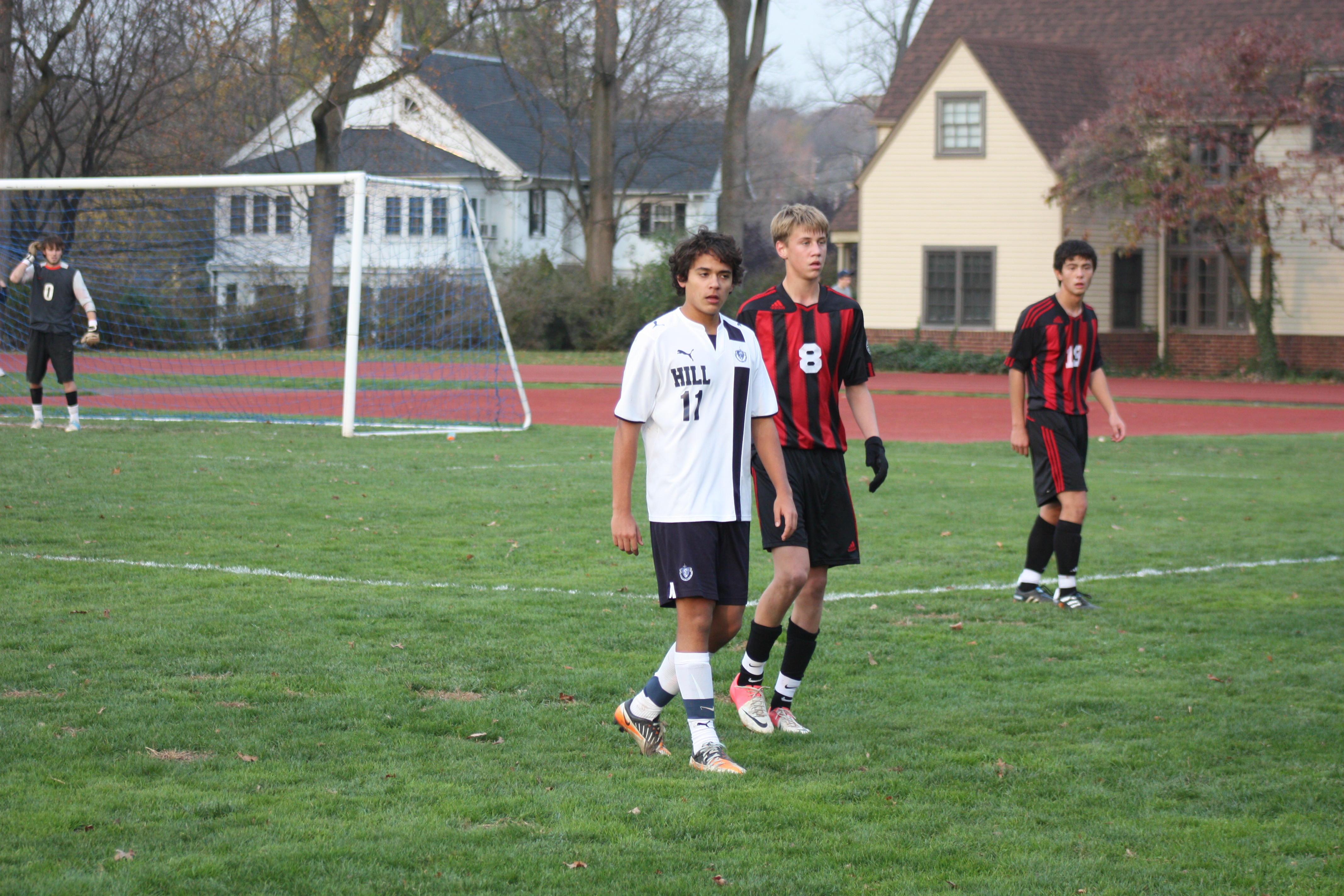Three male soccer players contest possession on a grass field during a game.