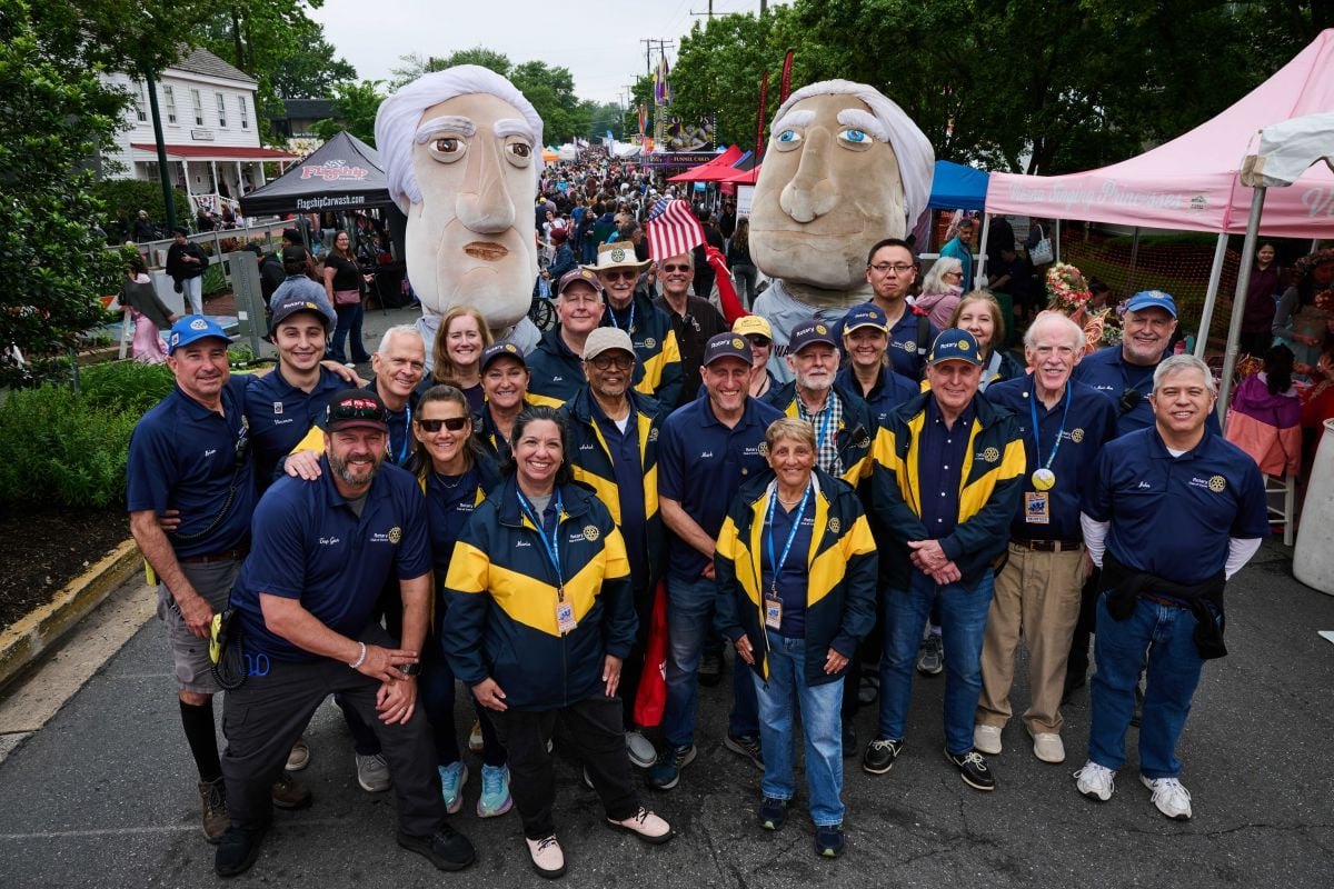 Large group in matching blue and gold jackets pose at a crowded outdoor street festival.