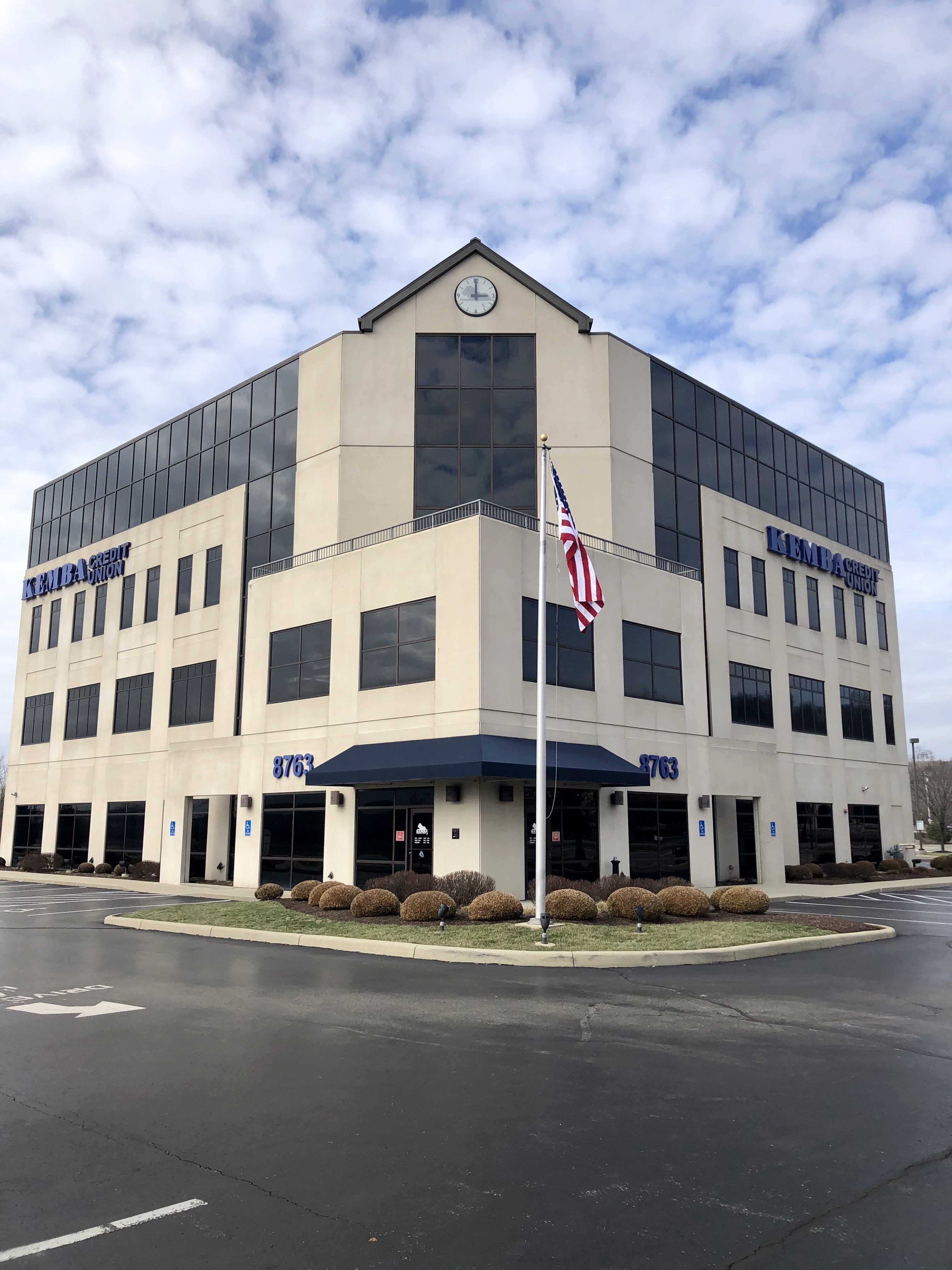 Four-story beige commercial office building with blue awnings and a flagpole.