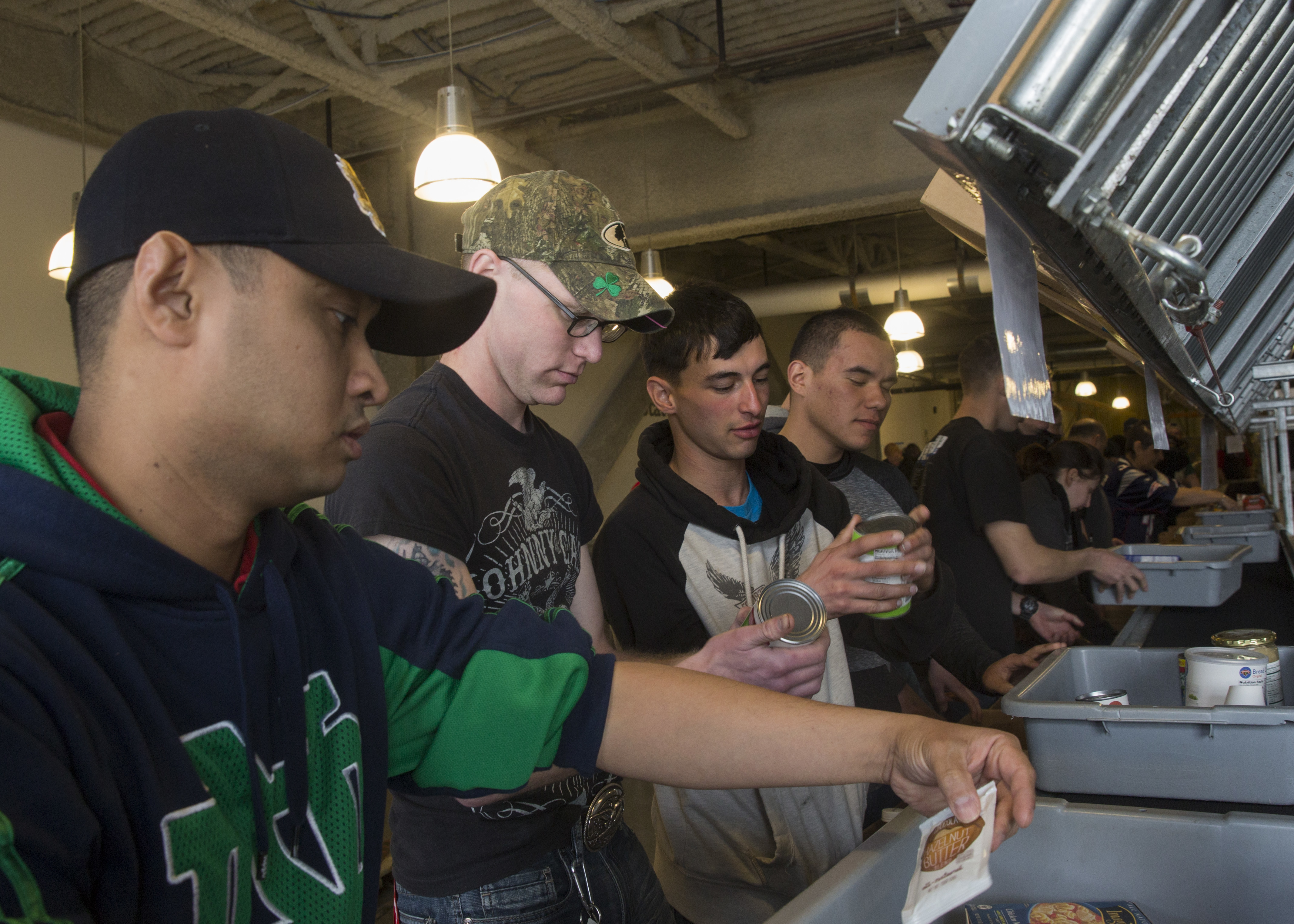 Volunteers stand at an indoor counter sorting and handling packaged food items.