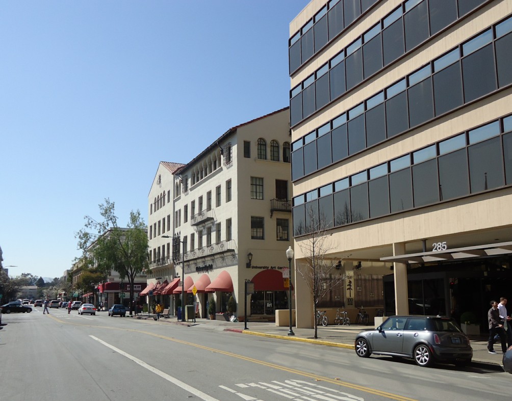 A downtown street with a glass office tower and older commercial buildings with red awnings.