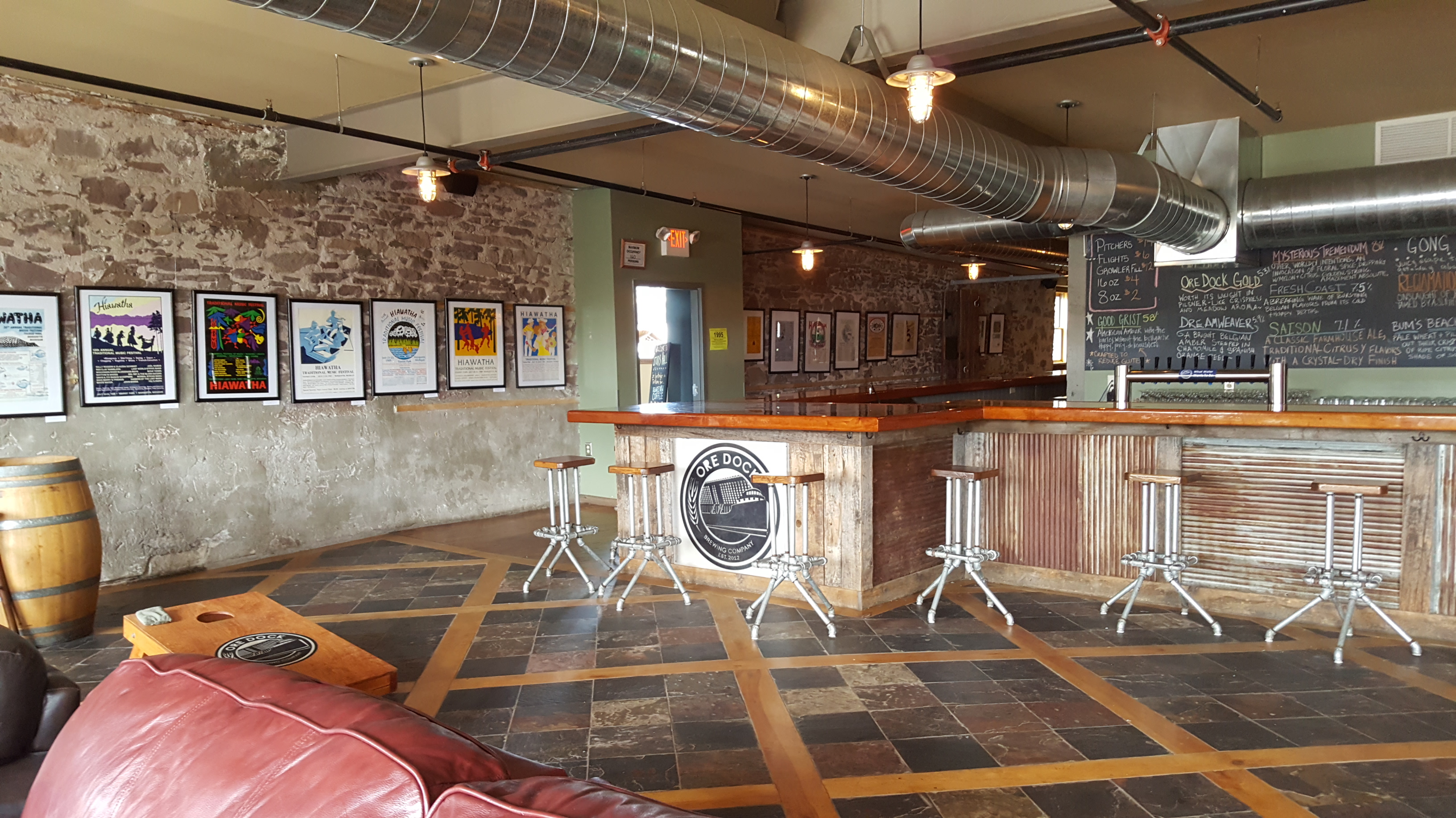 Brewery taproom interior with wooden bar, metal stools, and exposed brick walls.