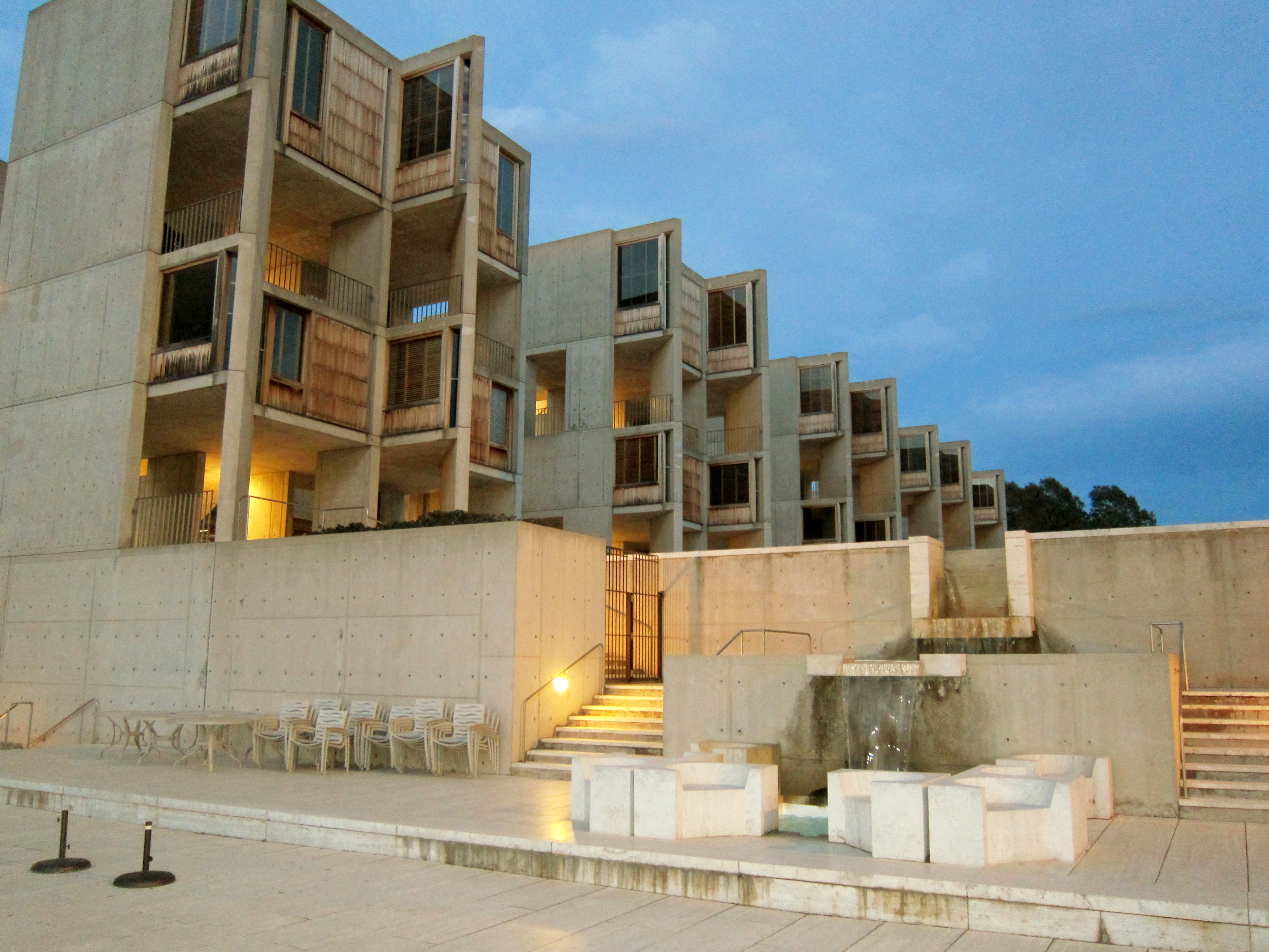 Brutalist concrete building at dusk with white chairs arranged on an open plaza.