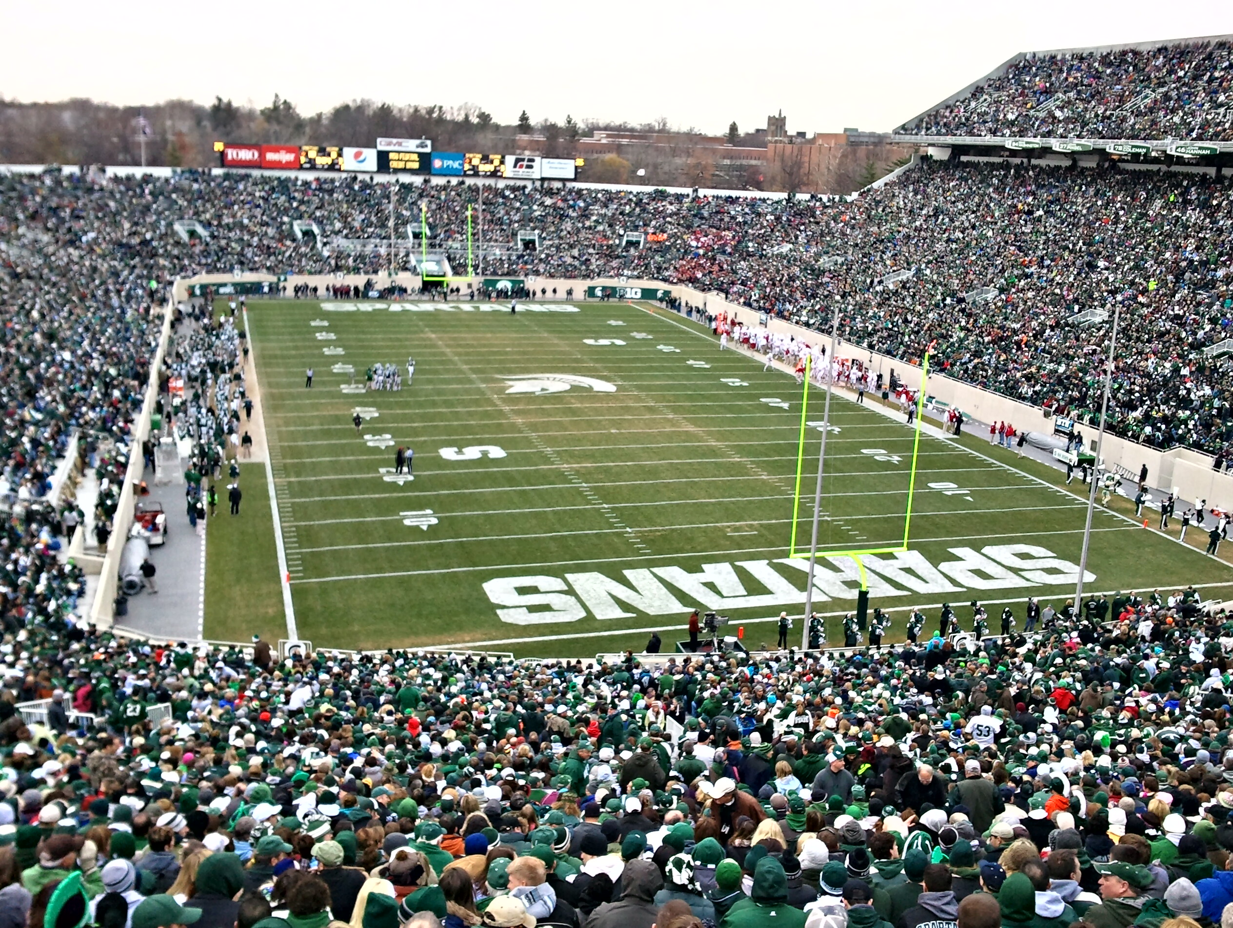 Packed football stadium with 'SPARTANS' in the end zone and yellow goalposts visible on the field.