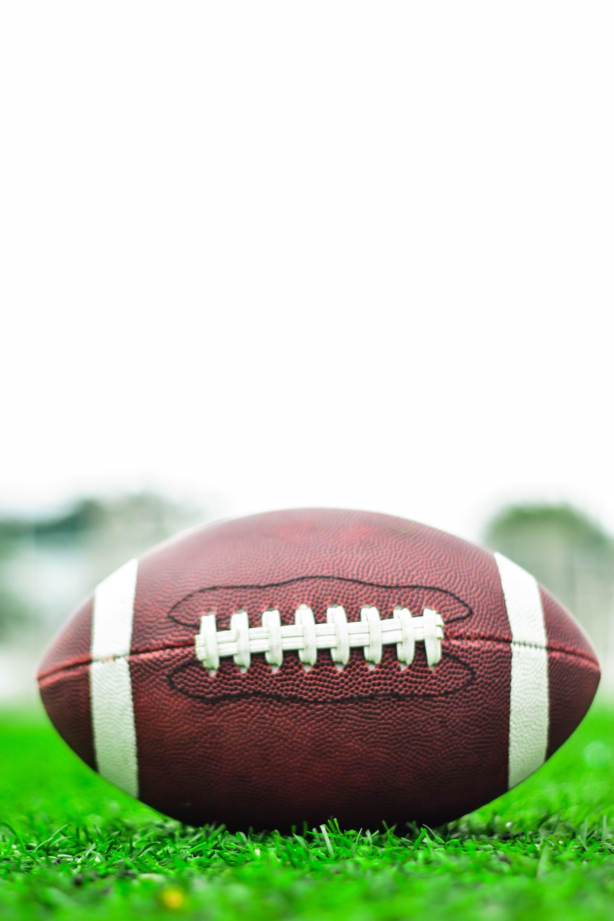 American football resting on lush green grass with clear sky background.