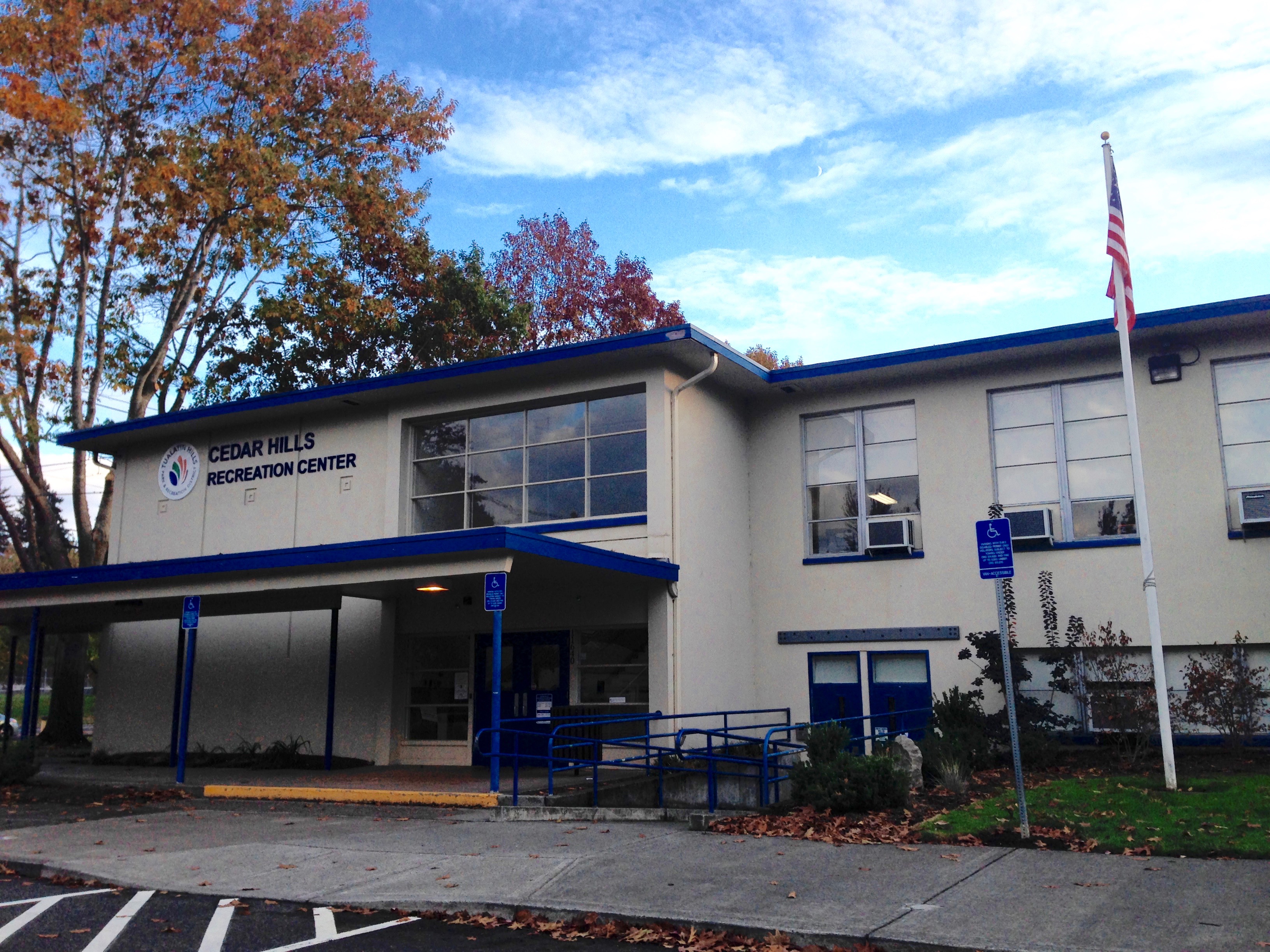 Two-story beige and blue recreation center building with flagpole and autumn trees