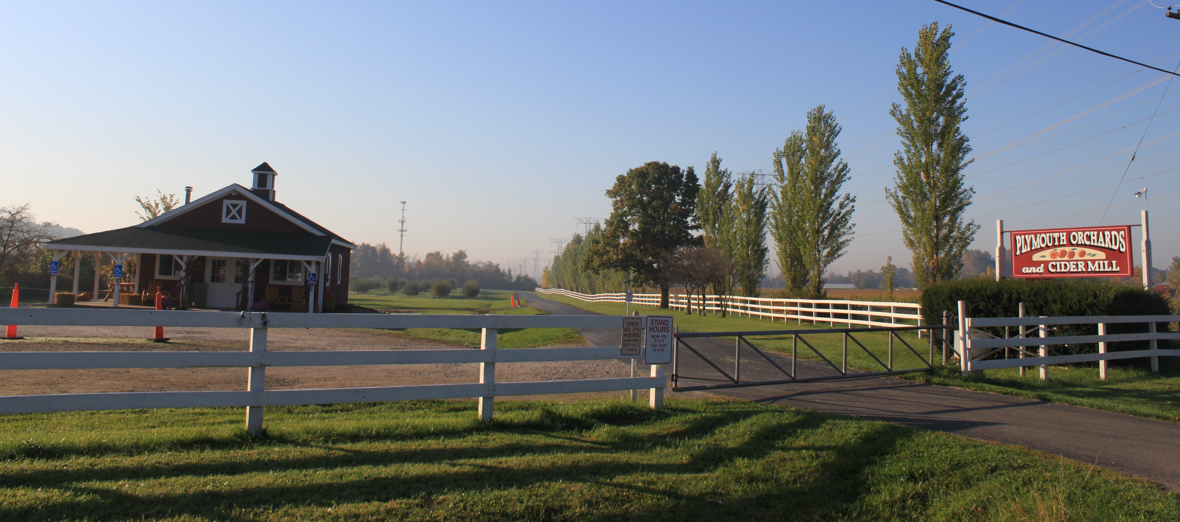 Entrance gate and red sign for Plymouth Orchards and Cider Mill, white fence and barn visible.