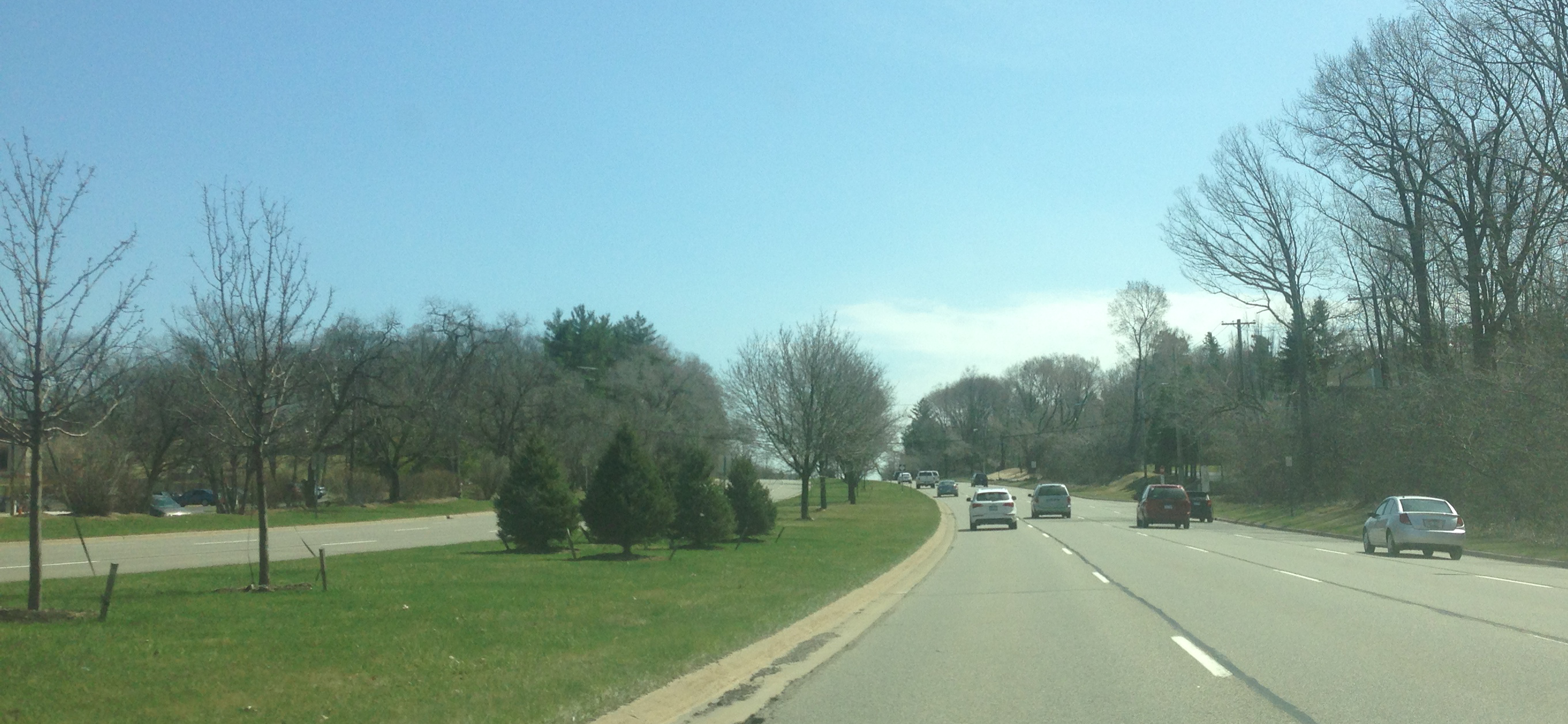 Multi-lane road with light traffic and tree-lined medians under a hazy blue sky.