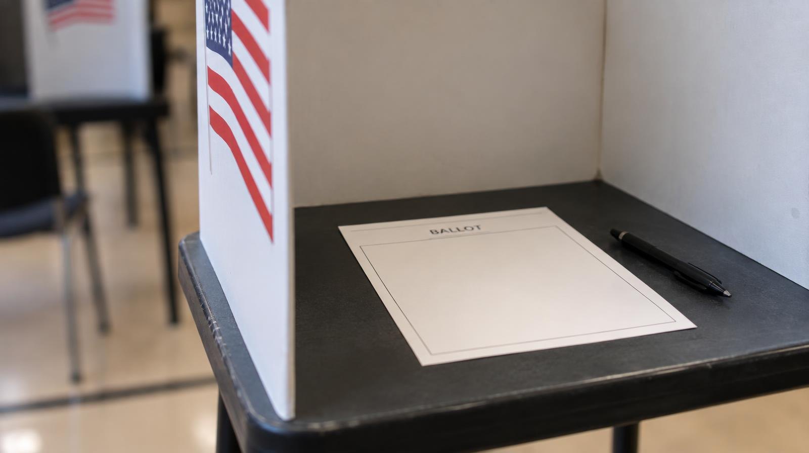 A blank paper ballot resting in a voting booth with a black pen beside it.