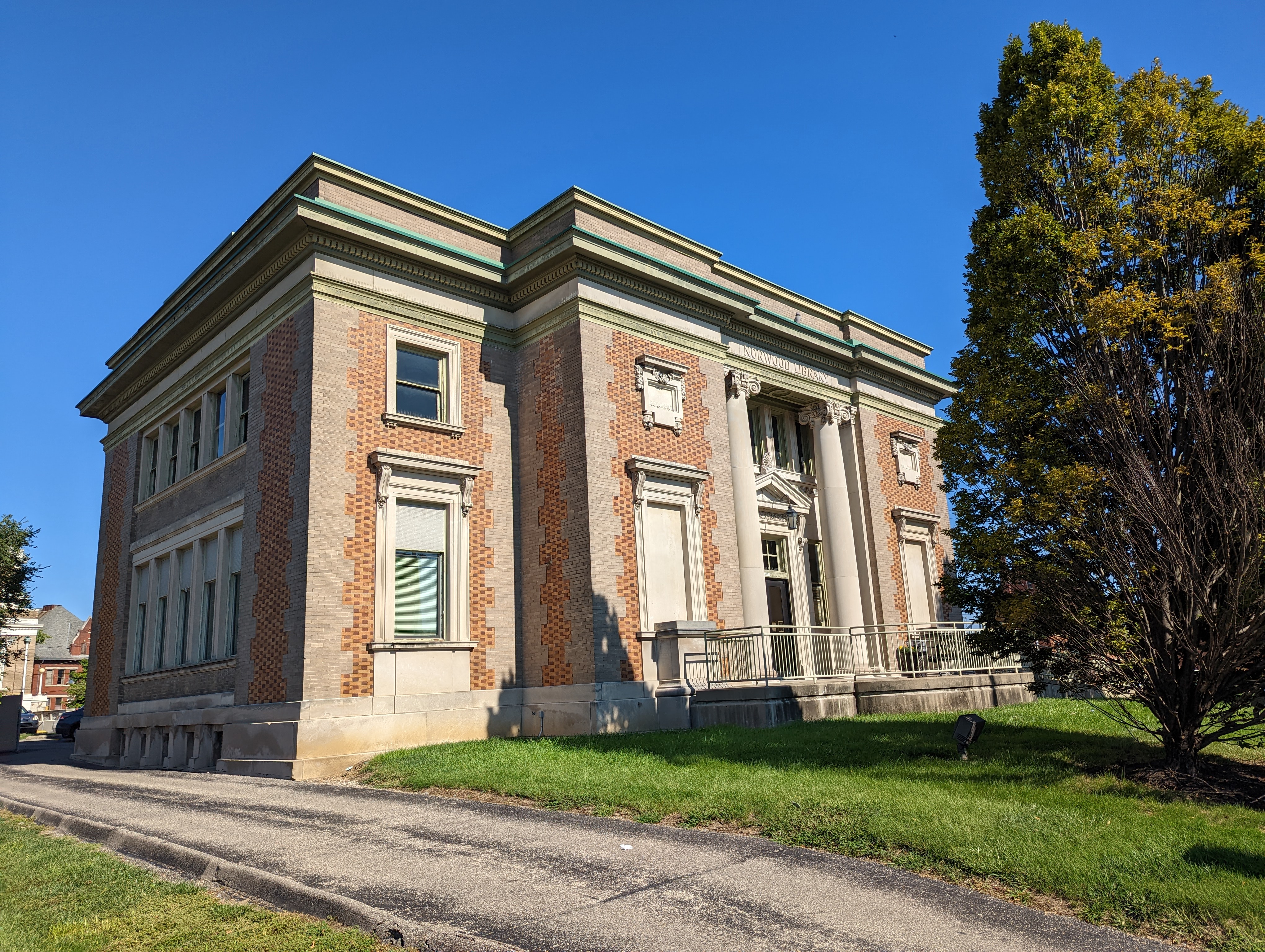 Red brick public library building with columned entrance and green lawn.