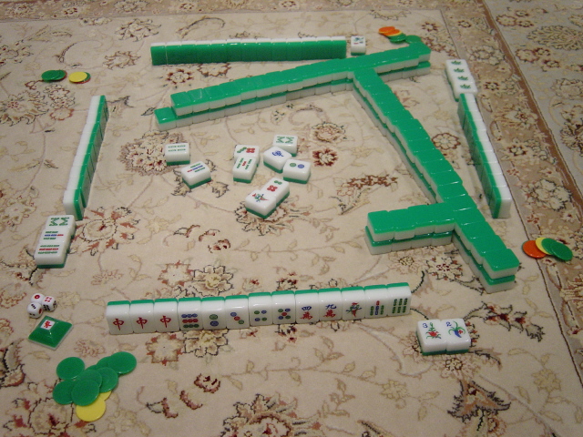 Mahjong tiles arranged in a square wall on a carpeted surface with colored scoring chips.