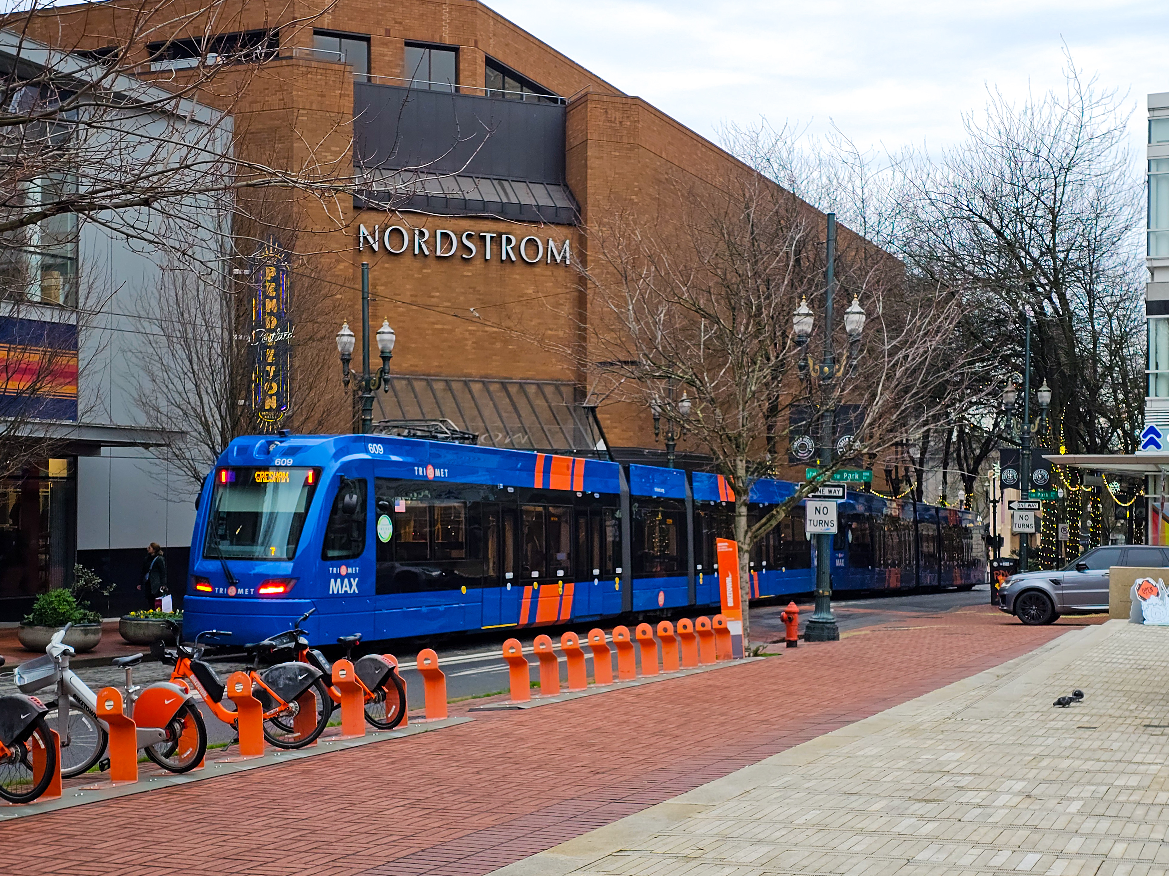 A blue and orange MAX light rail train moves along a downtown Portland street.