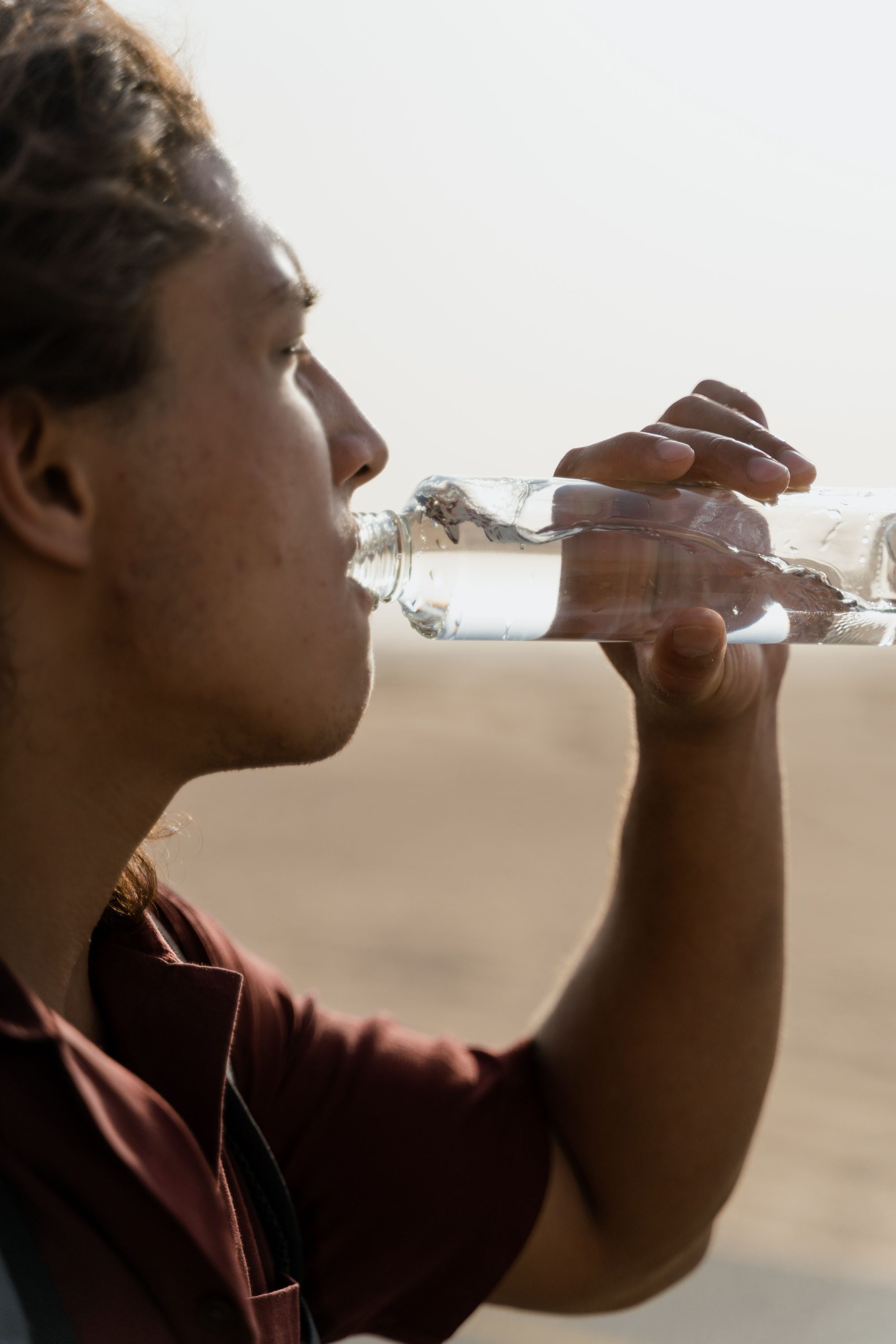 Close-up of a man drinking water from a bottle in an outdoor setting.