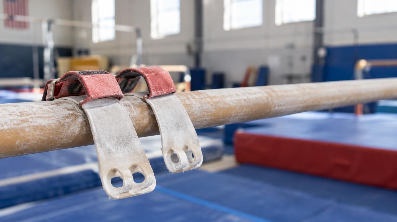 Gymnastics hand grips resting on a chalk-dusted horizontal bar above a colorful mat.