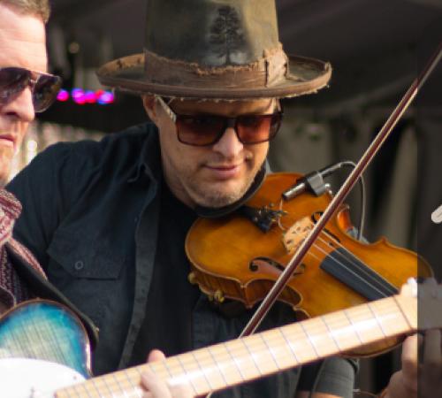 Two musicians performing on stage, one playing a fiddle and one playing an electric guitar.