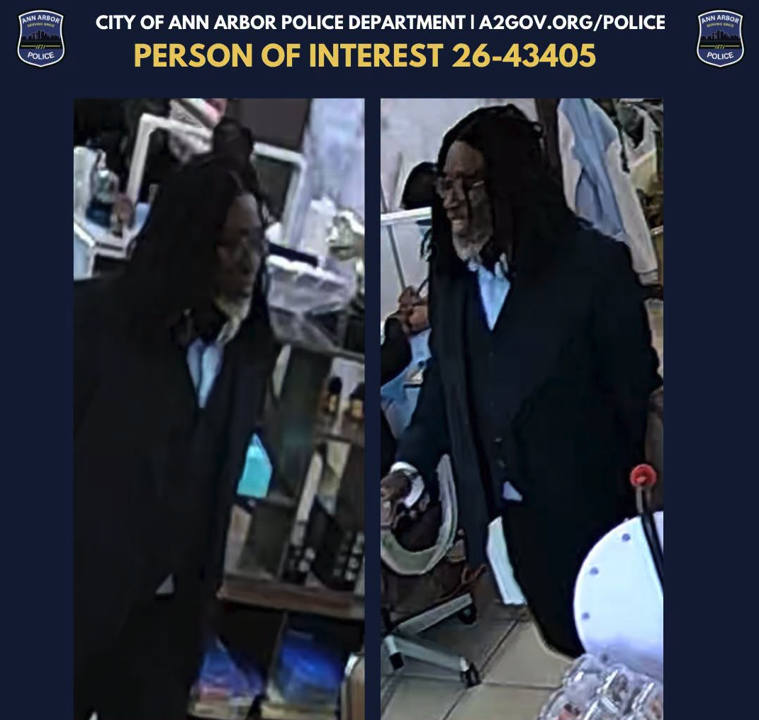 A police bulletin from the Ann Arbor Police Department showing two surveillance camera stills of a man with long dark hair, glasses and a dark coat inside a store, labeled "Person of Interest 26-43405."