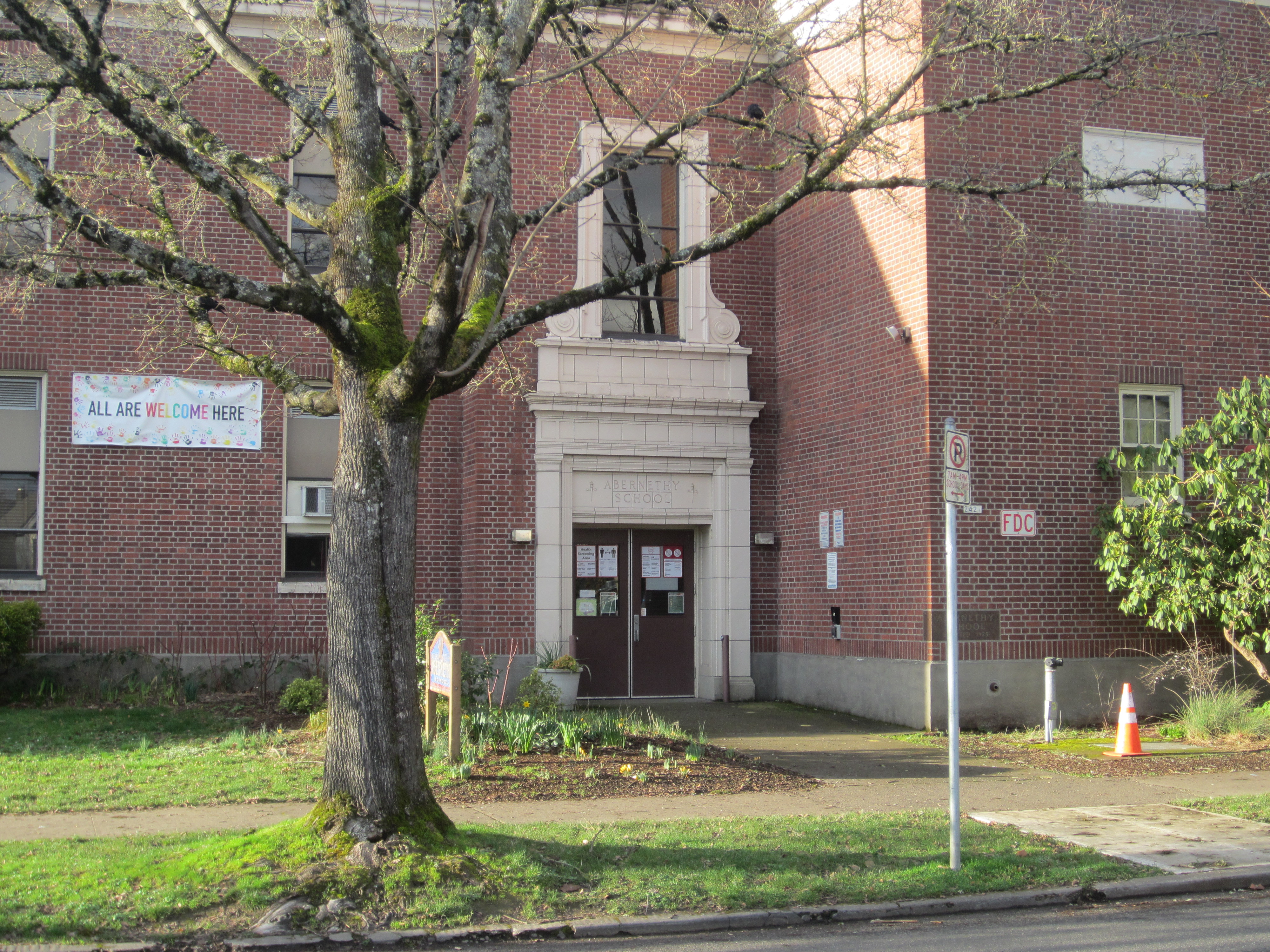 Red brick school building with a welcoming banner in a window and a bare tree in front.